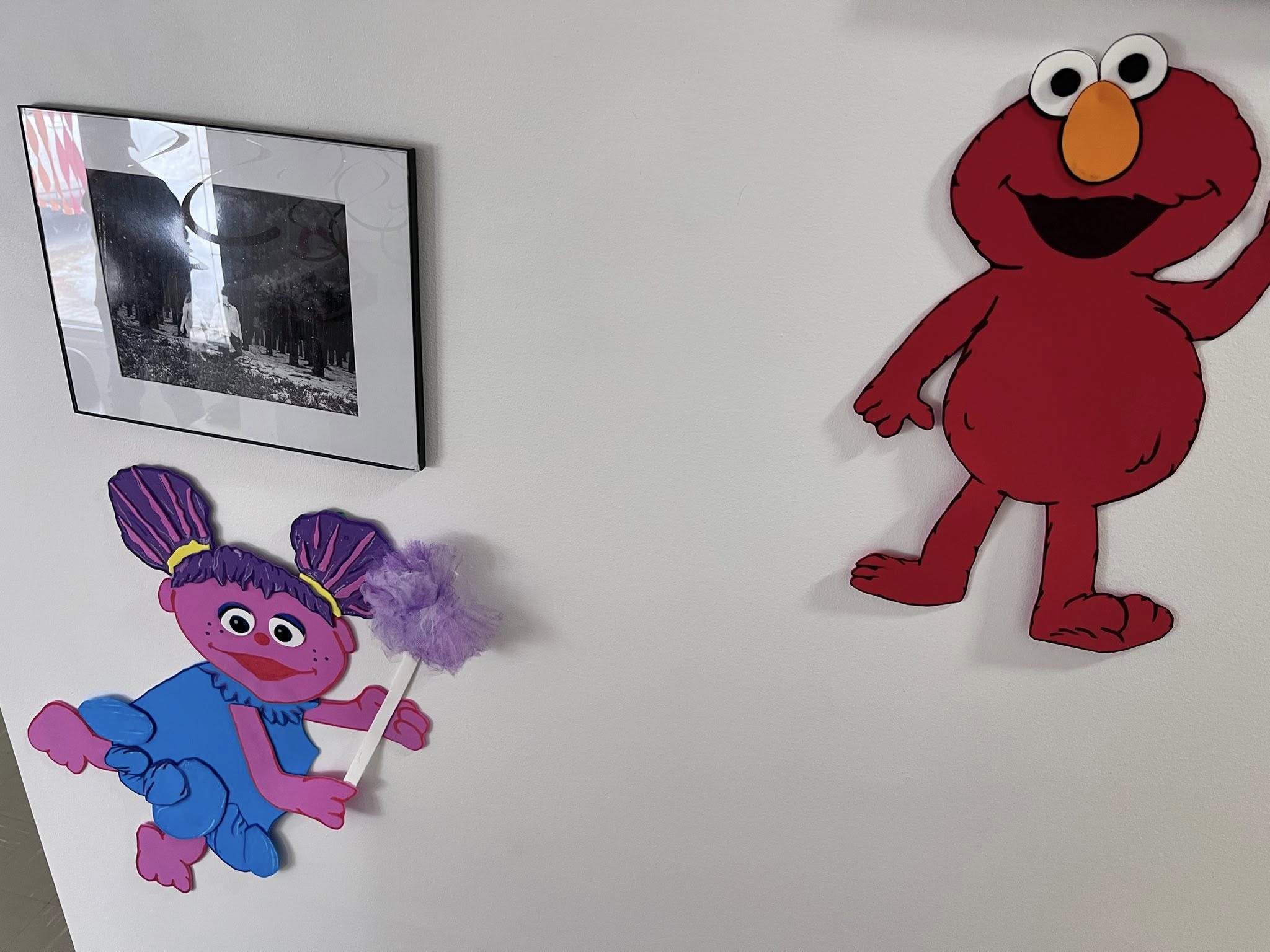 Wall decor of Sesame Street characters Abby Cadabby and Elmo next to a framed black and white photograph.