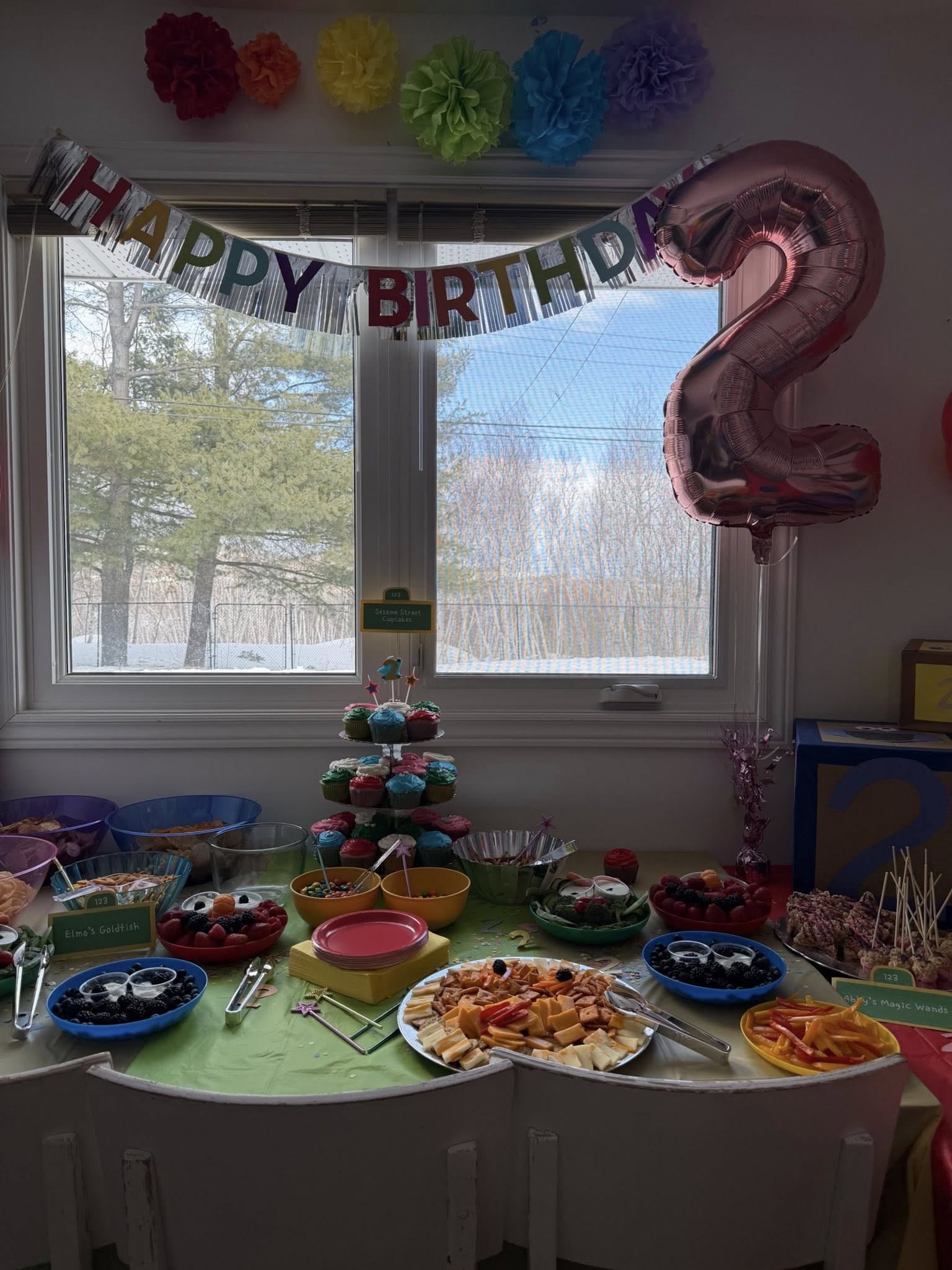 Table spread with Sesame Street themed snacks, cupcakes, and party decorations for a second birthday celebration.