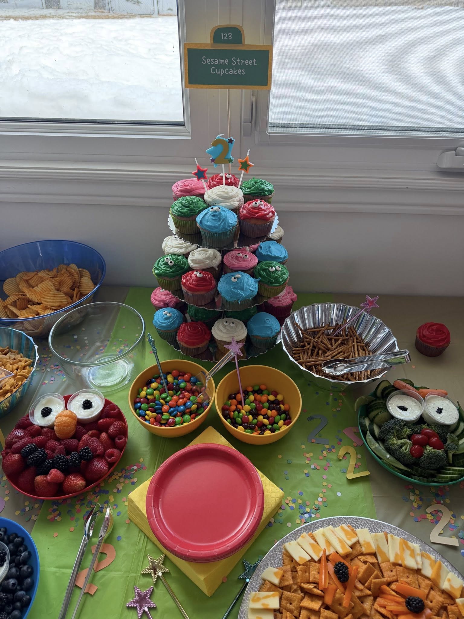 Sesame Street birthday party snack table with colorful cupcakes, fruit platter, candy, and cheese and cracker tray.