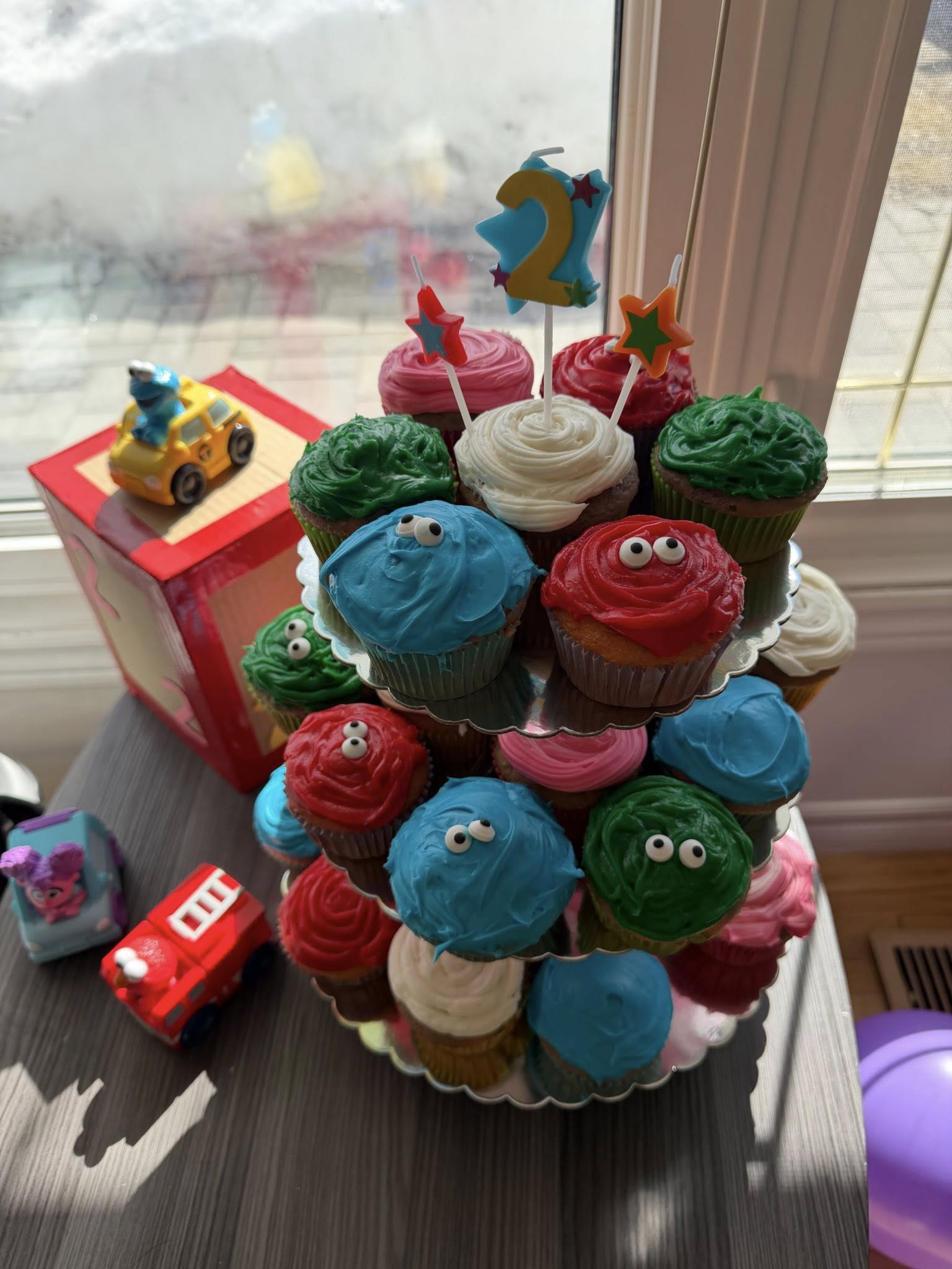 Tiers of colorful cupcakes decorated into monsters with candy eyes for a second birthday party.
