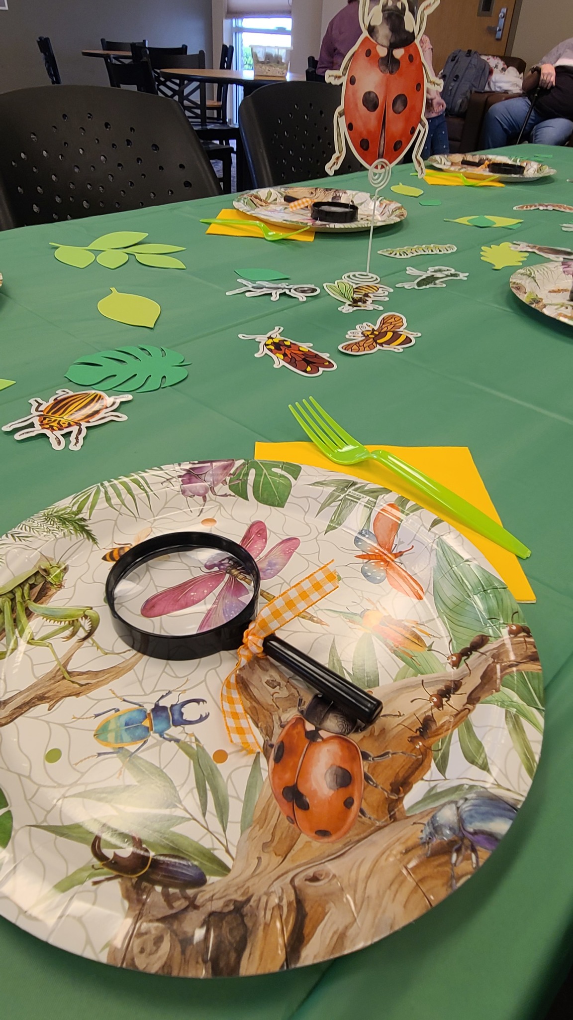 Table setting with bug-themed paper plates, magnifying glasses, and insect cutouts for a nature-themed party.