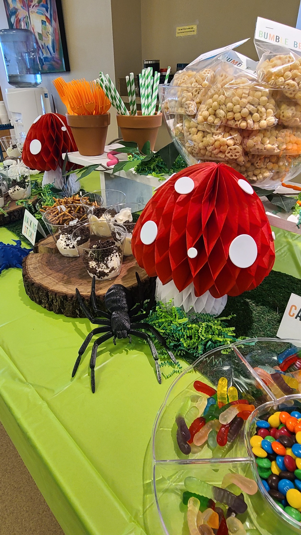 Table decorated with woodland-themed party treats including snacks, candy, paper mushroom accents, and a toy spider.