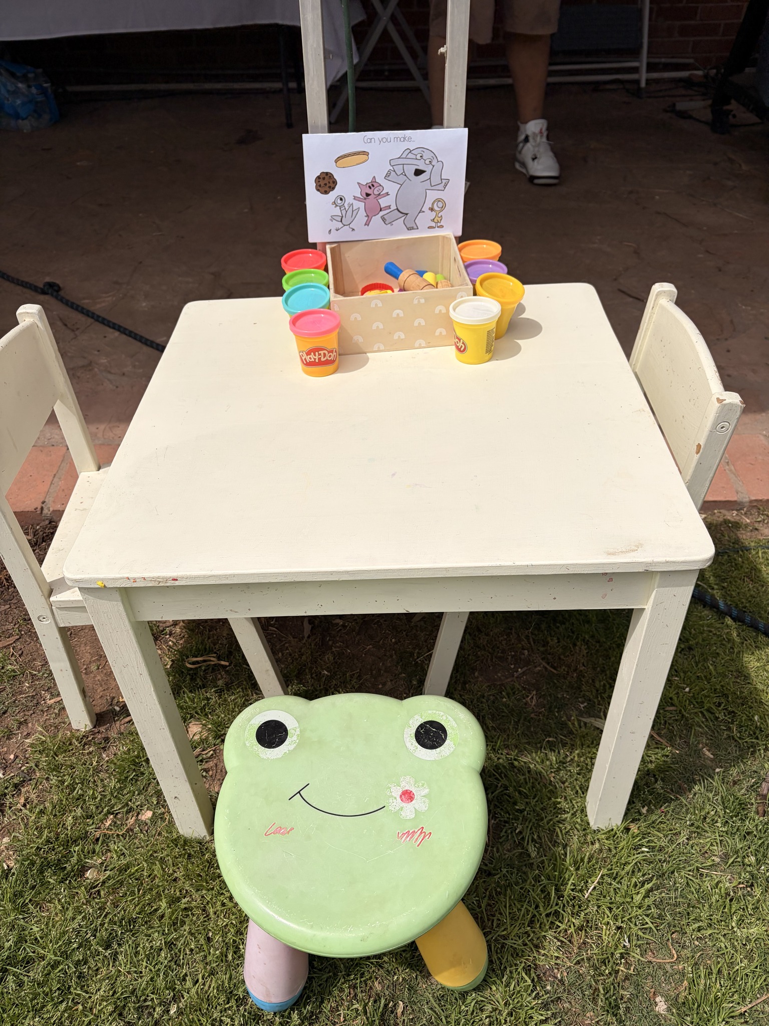 Toddler activity table with Play-Doh cups and a frog-shaped stool on grass