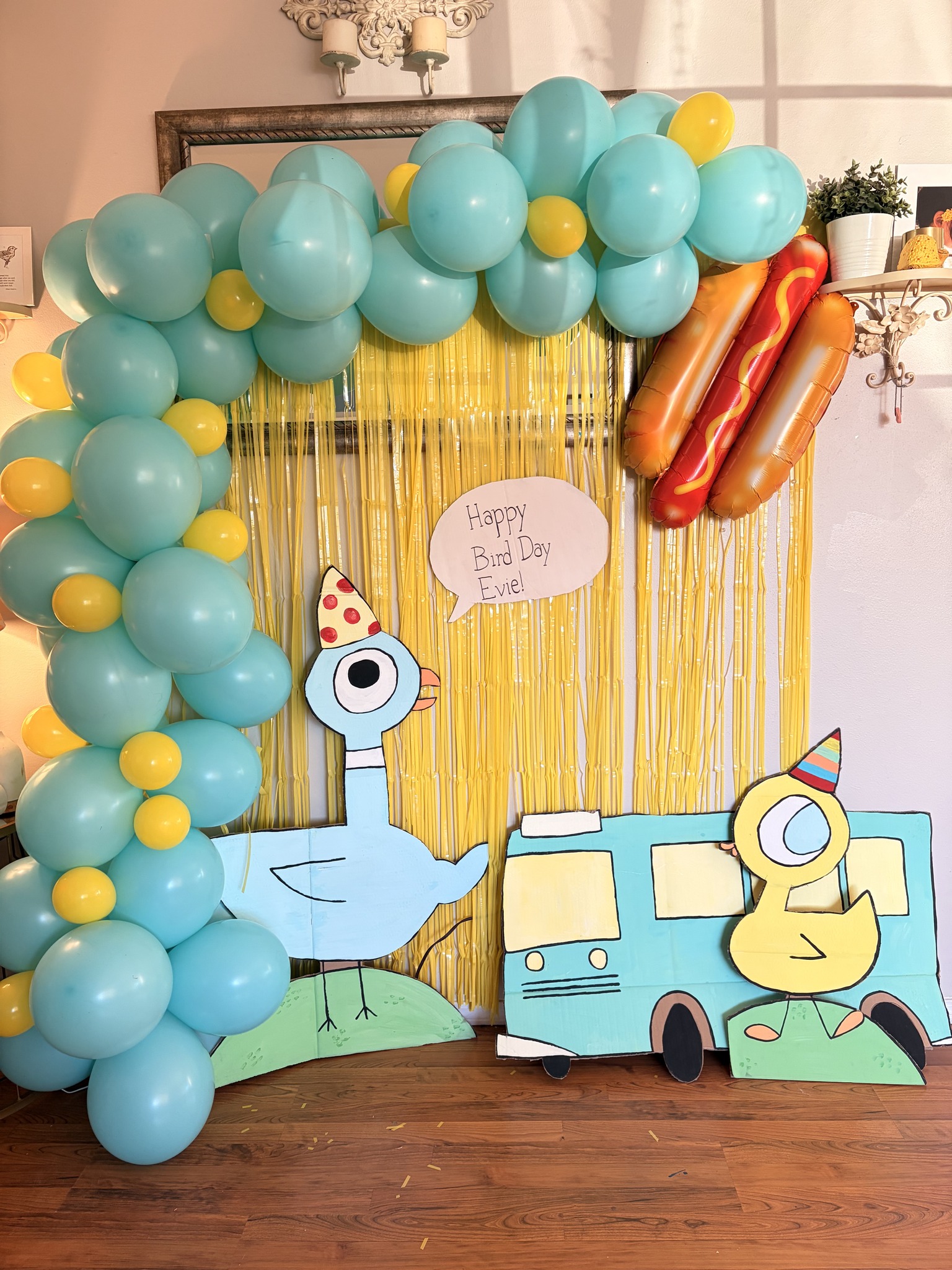 Birthday party backdrop featuring blue and yellow balloons, a Pigeon theme decoration, and a hot dog balloon.