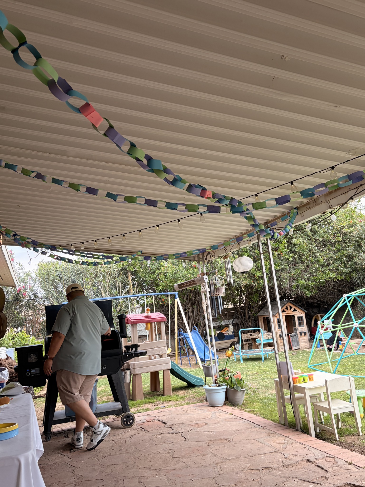 Man standing at a backyard grill under a patio cover decorated with paper chains
