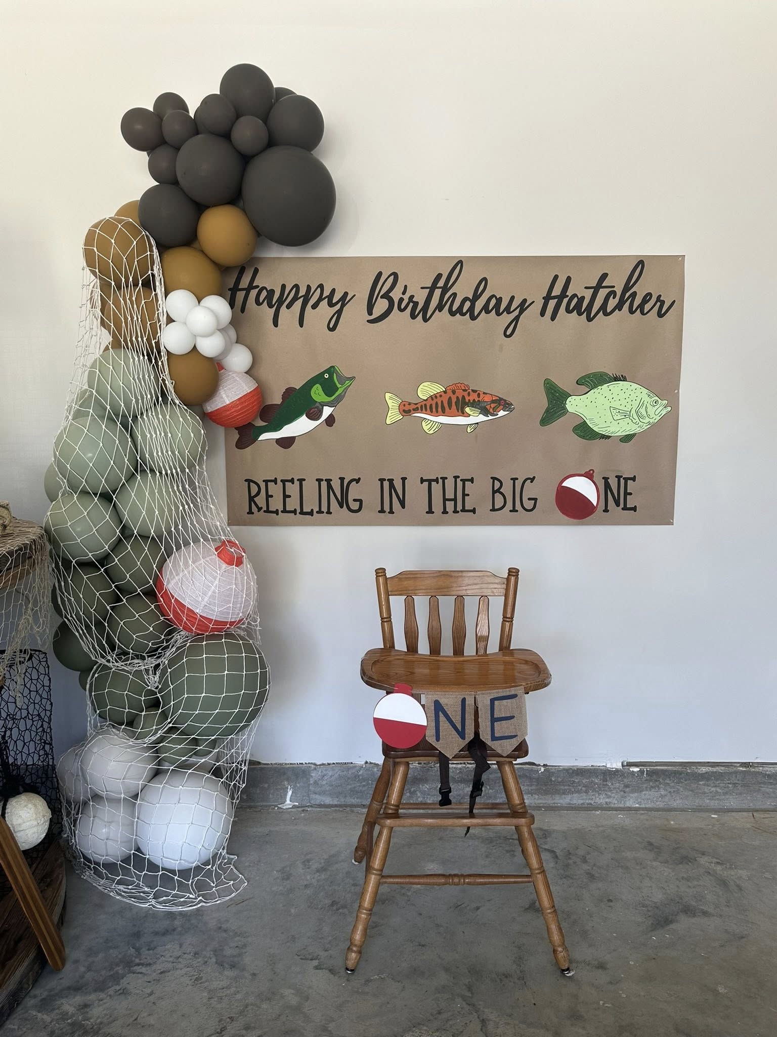 Fishing themed first birthday party decoration with a balloon arch and a sign labeled Reeling in the Big One.