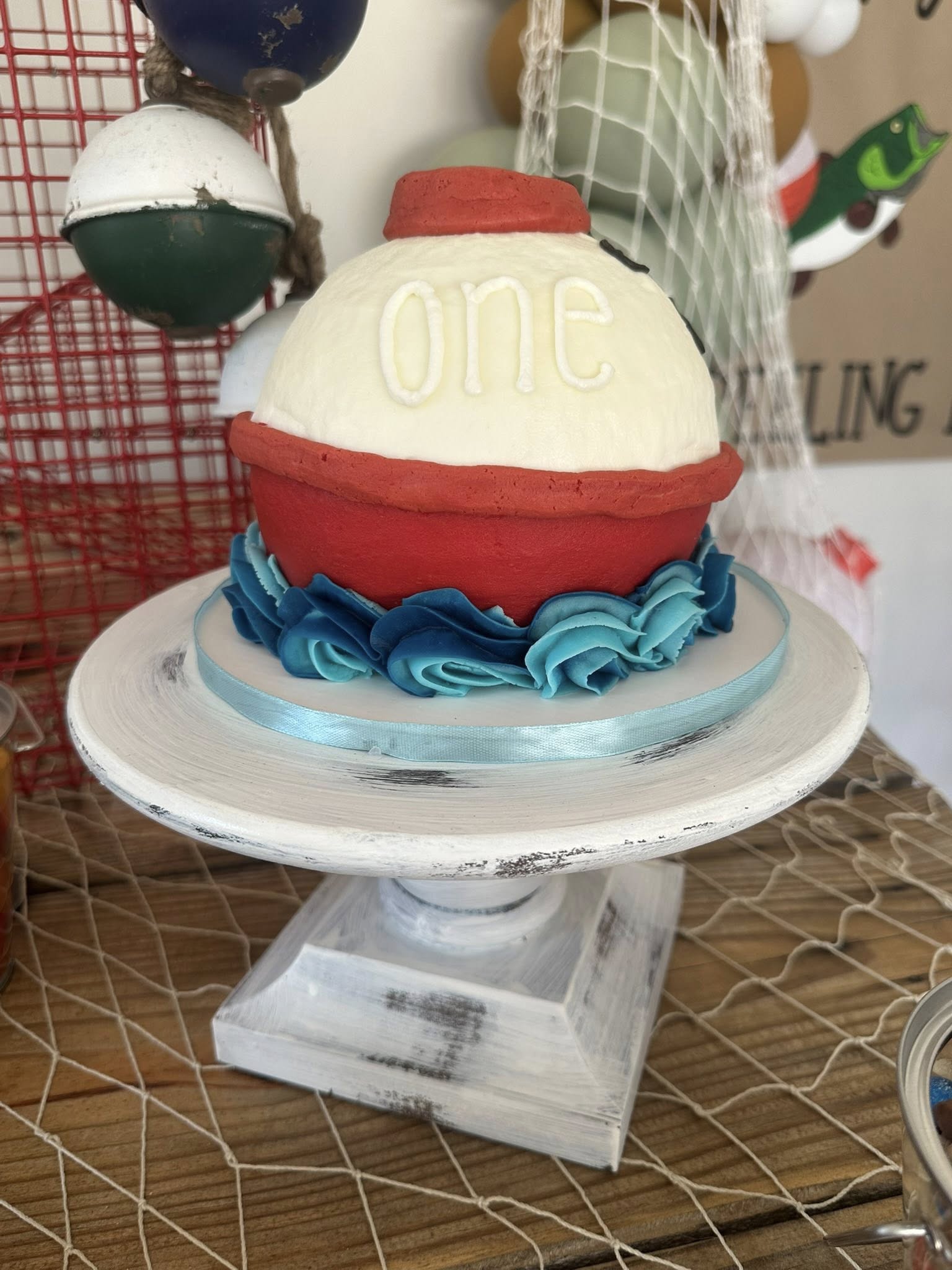 First birthday cake decorated like a red and white fishing bobber on a rustic cake stand