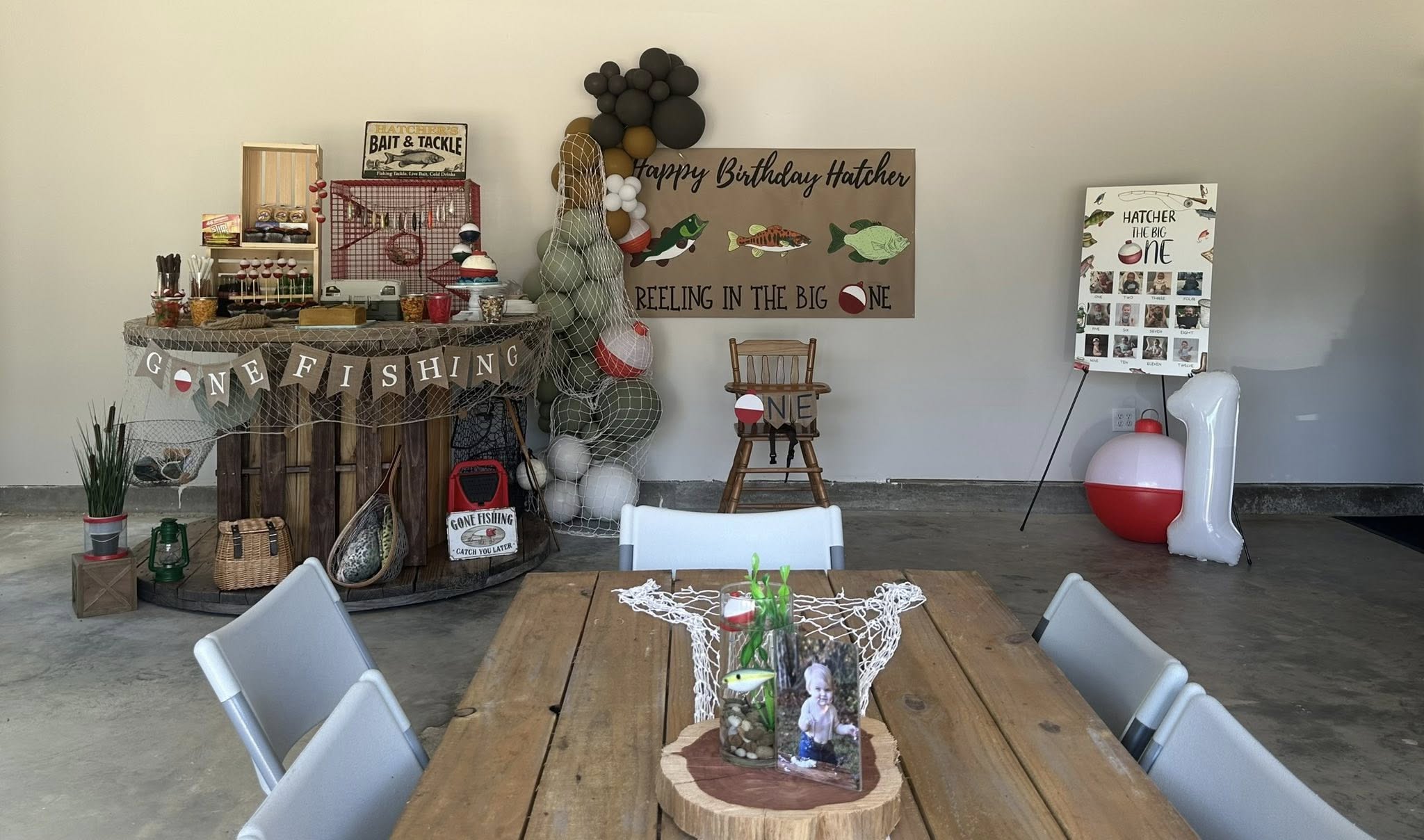 Fishing-themed first birthday party setup featuring a snack table, 'Reeling in the Big One' banner, and photo board.