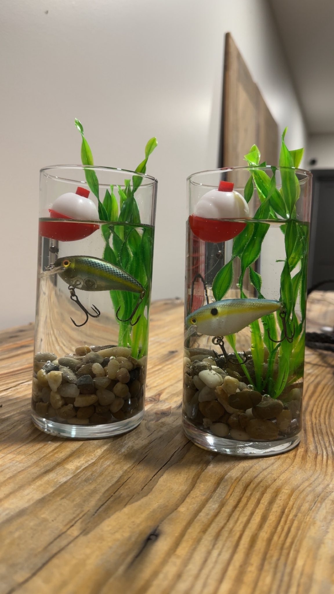 Two cylindrical vases decorated as fishing scenes with gravel, plastic plants, fishing lures, and bobbers.