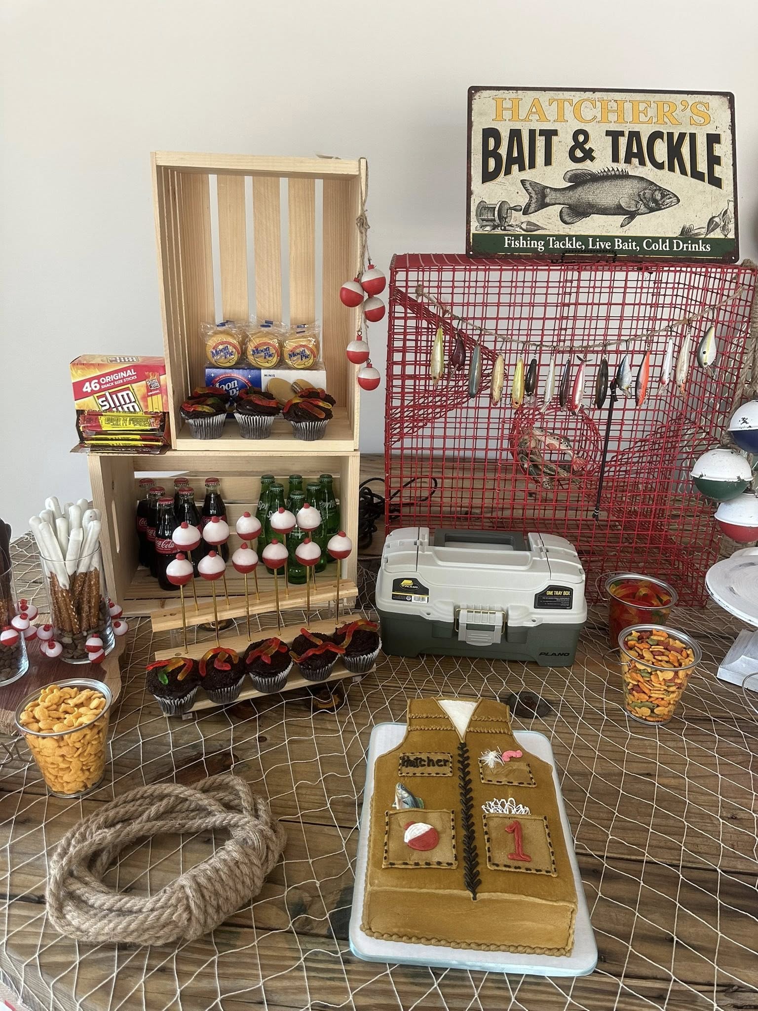 Fishing themed party dessert table featuring a tackle vest cake, bobber cake pops, fishing lures, and snacks.