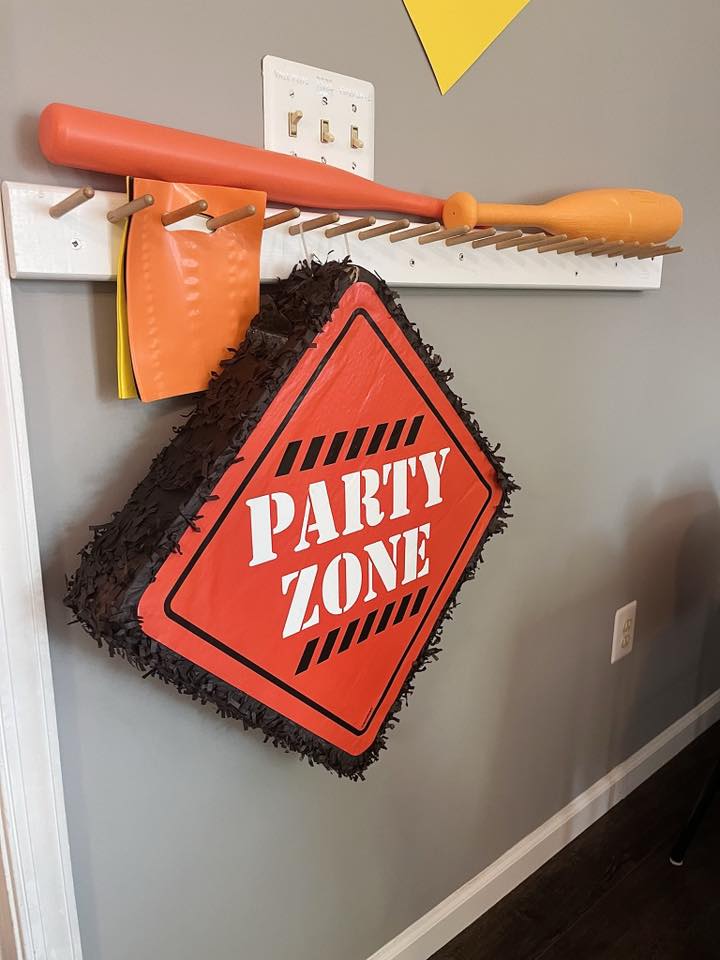 Construction-themed Party Zone piñata hanging on a rack with an orange plastic baseball bat.