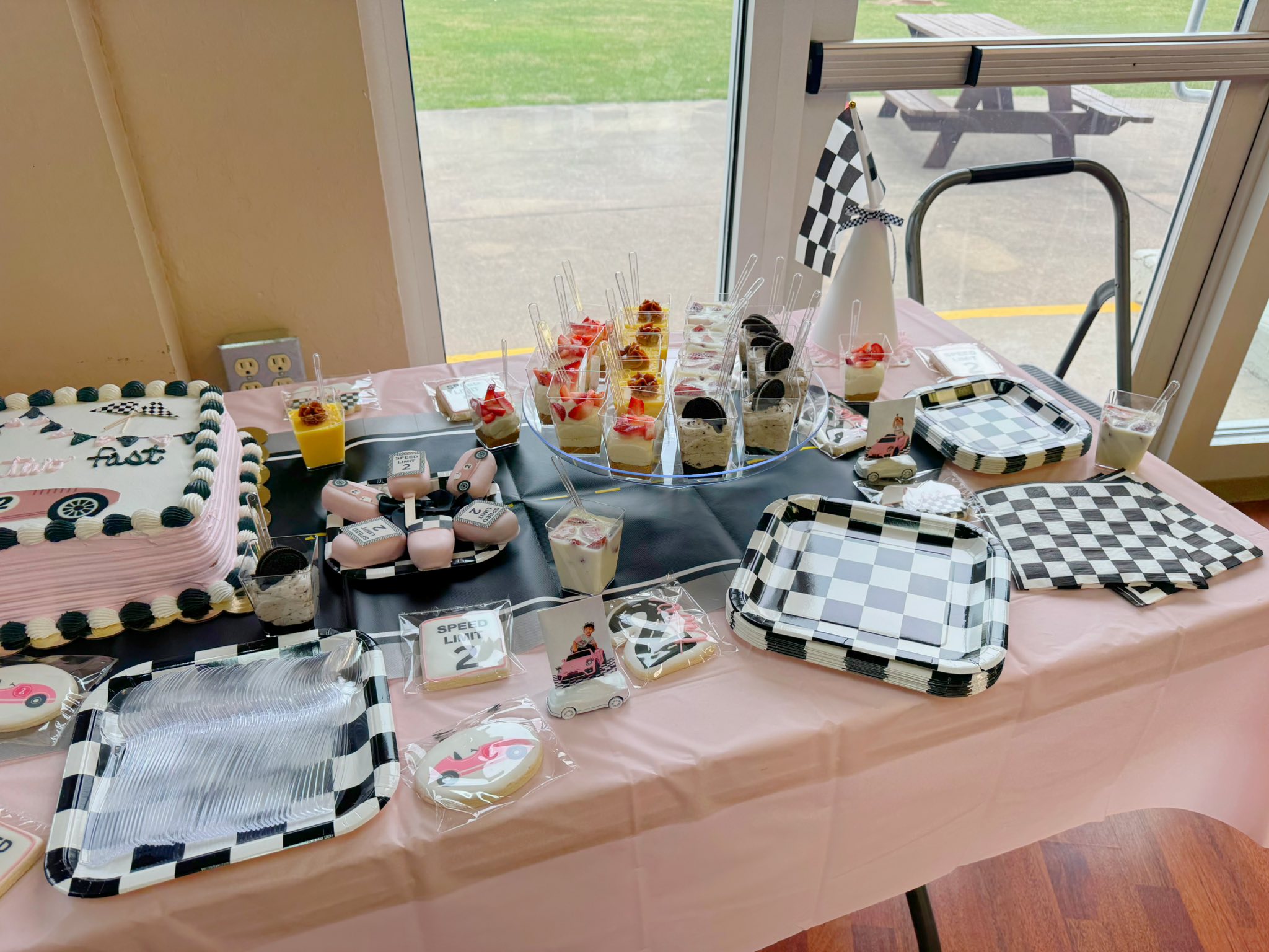 Race car-themed birthday party dessert table featuring a pink cake, checkered plates, and custom cookies.