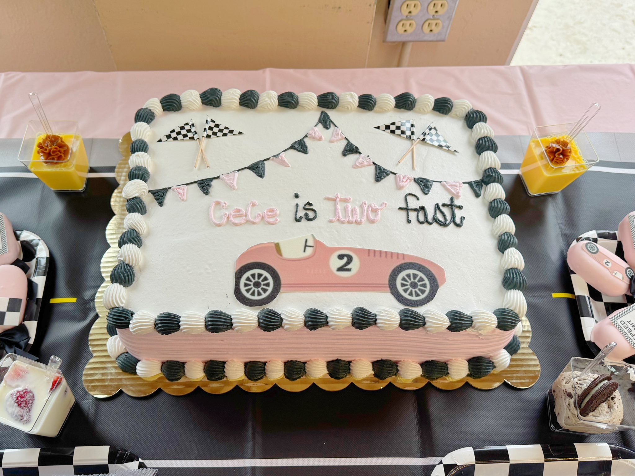 Rectangular sheet cake decorated with a pink race car, checkered flags, and the text Cece is Two fast.