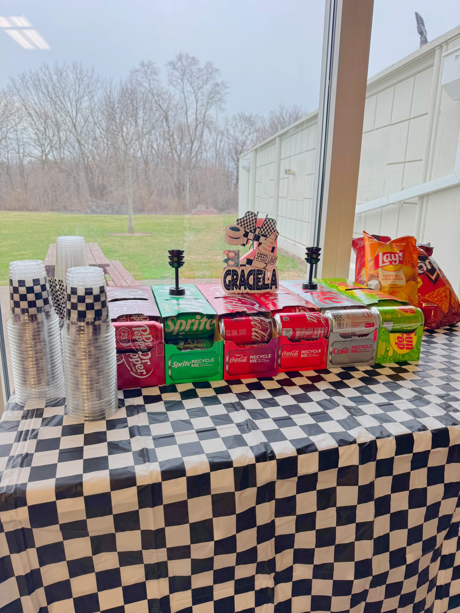 Race car-themed party snack table with soda packs, checkered tablecloth, and a personalized sign for Graciela.