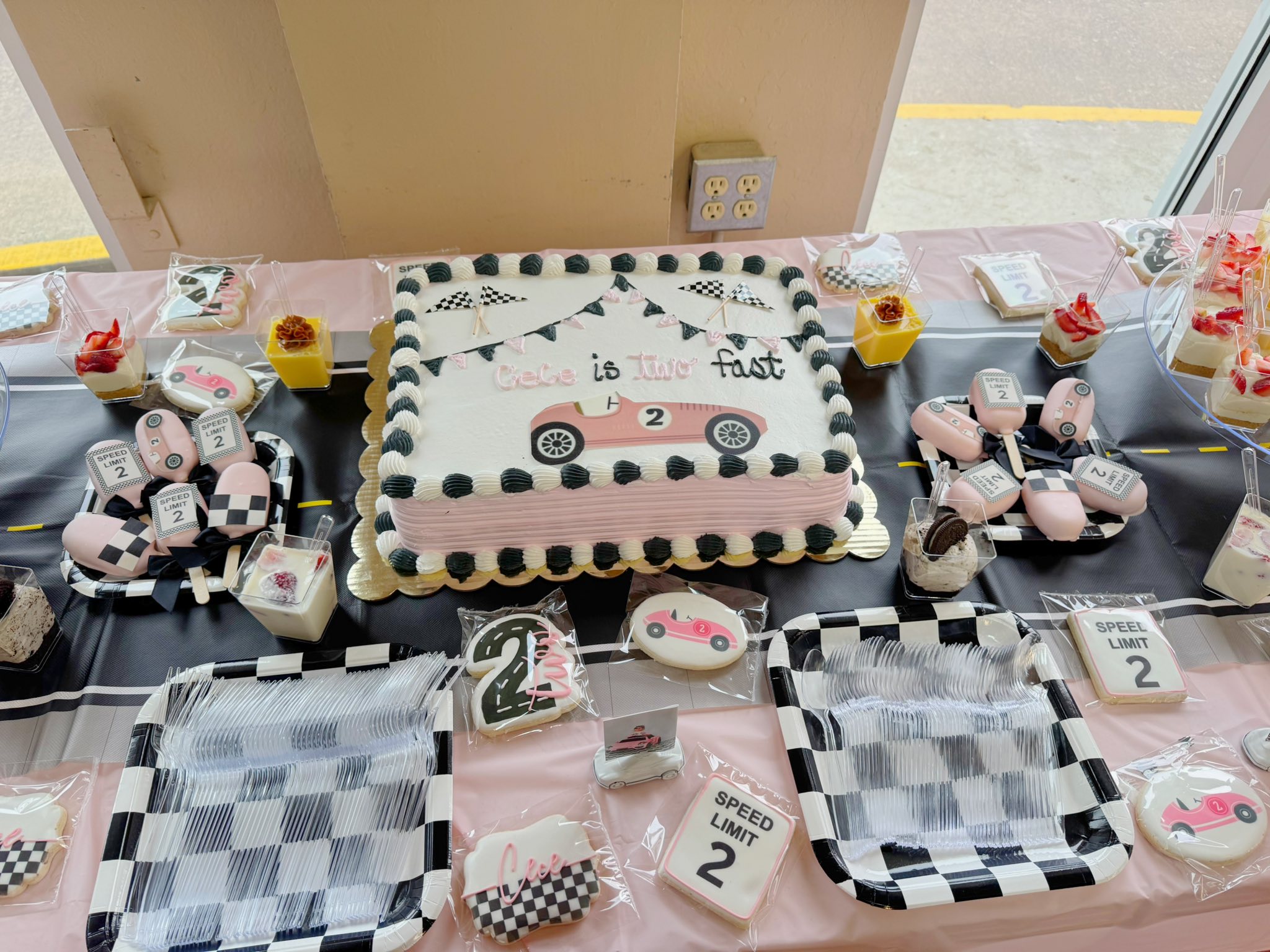 Race car-themed second birthday dessert table featuring a custom cake, checkerboard plates, and personalized cookies.