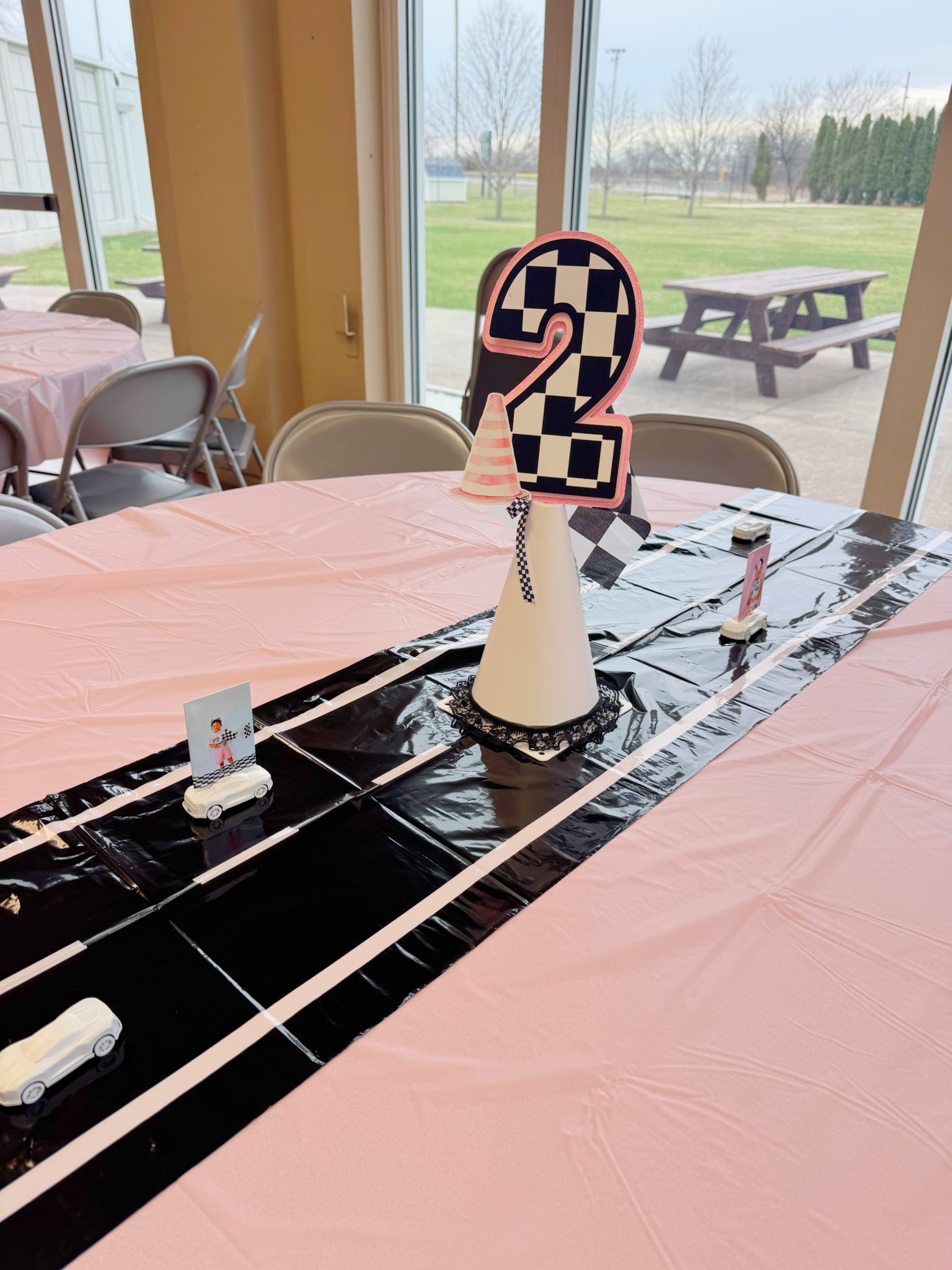 Race car-themed second birthday centerpiece on a light pink tablecloth with a black road runner.
