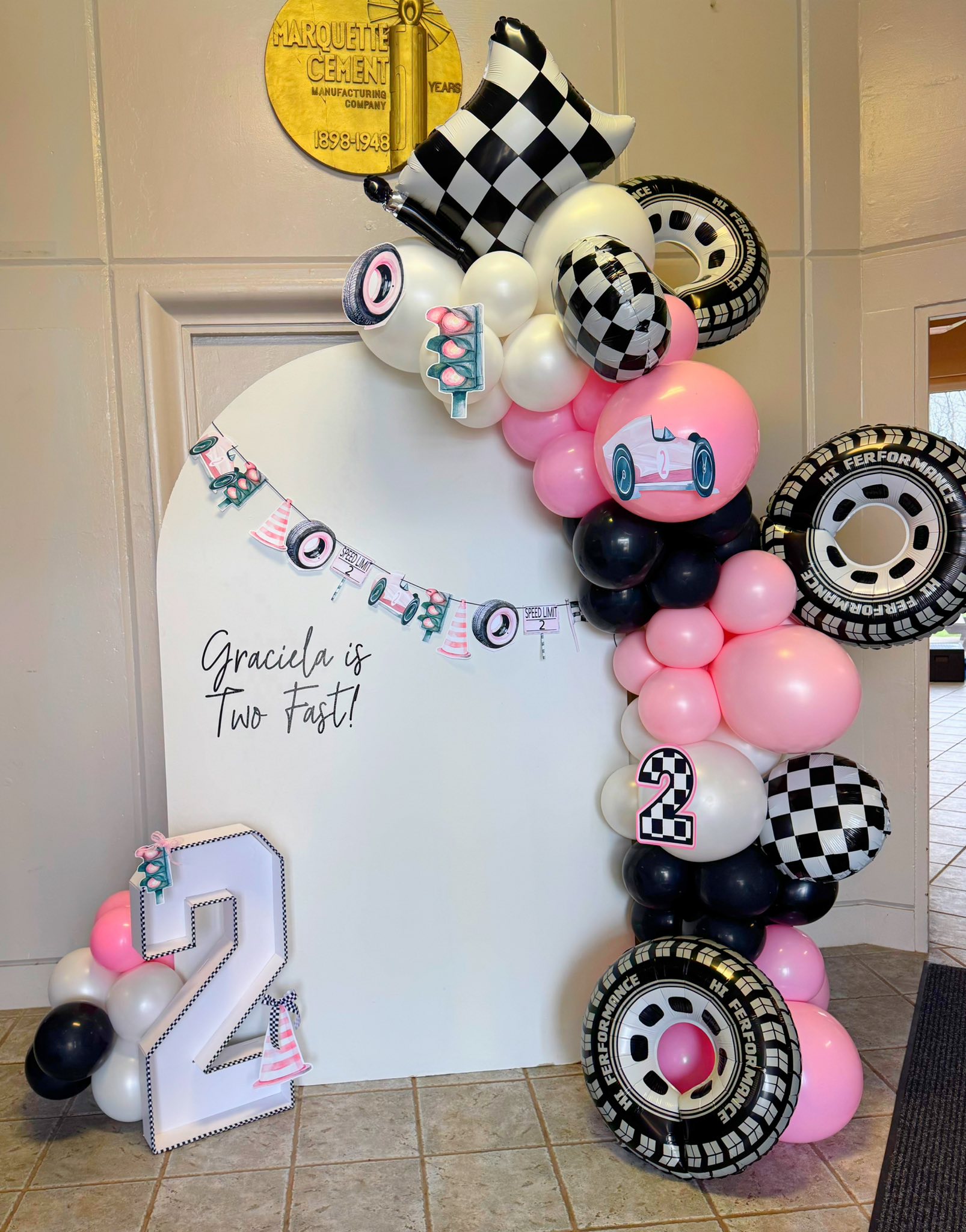 Racing themed balloon arch and backdrop for Graciela's second birthday with race car and tire decorations.