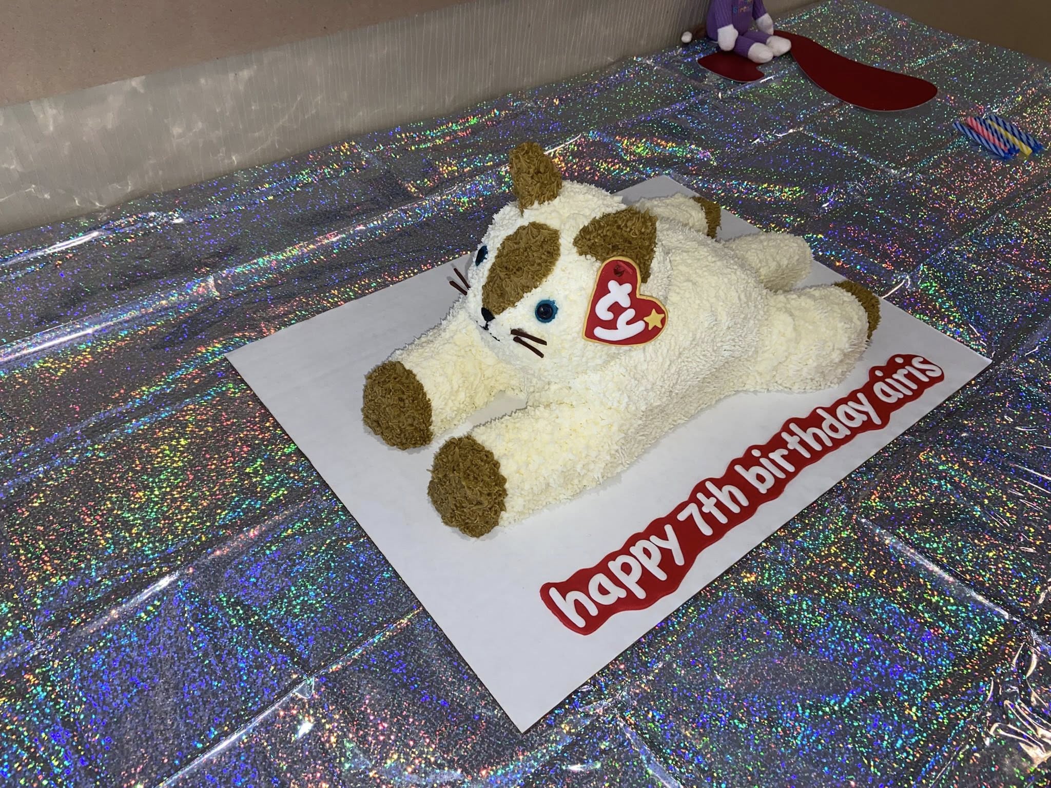 Cat-shaped birthday cake decorated to look like a plush toy with a Ty tag that says happy 7th birthday Airis.