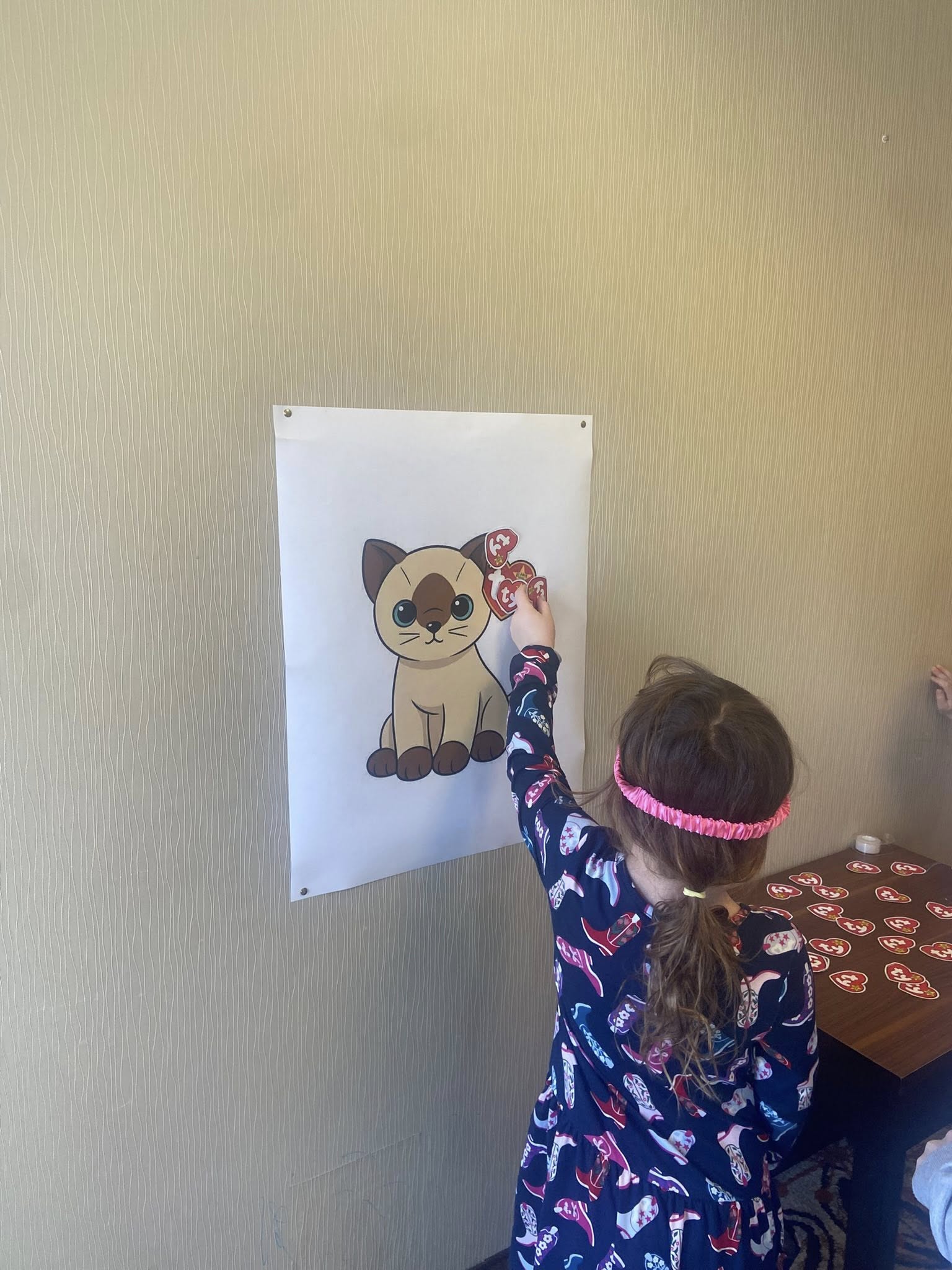 Child playing a pin the tag on the cat game with a Siamese cat poster