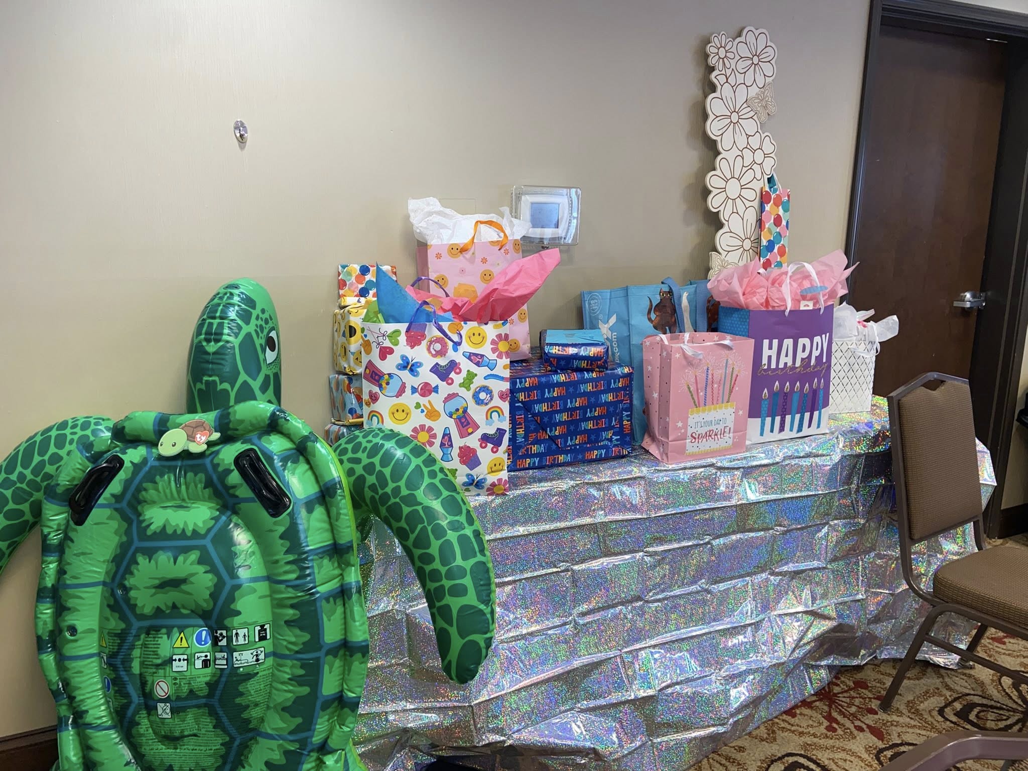 A festive gift table with colorful birthday gift bags and a giant inflatable sea turtle decoration.