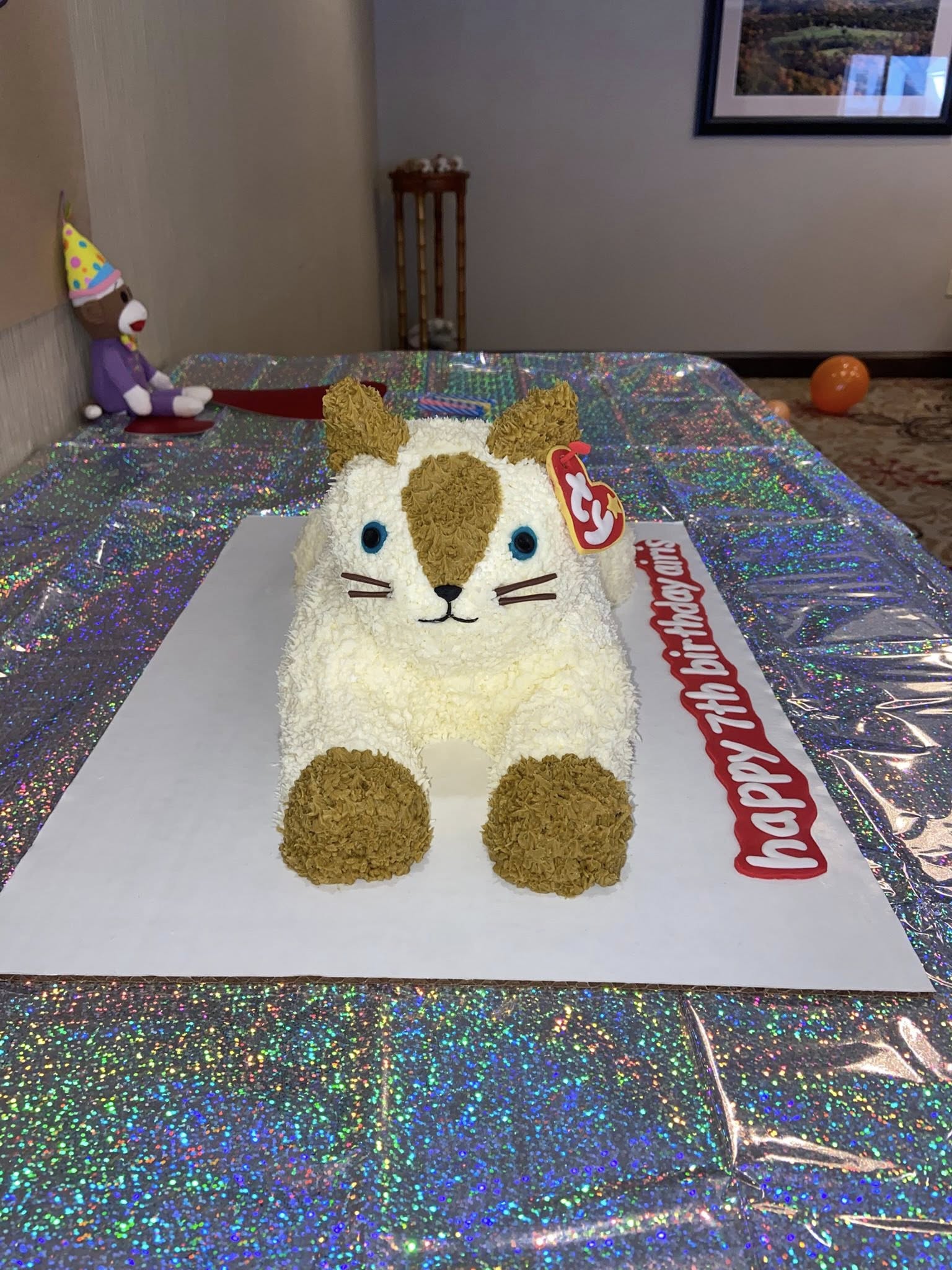 Cat-shaped birthday cake decorated with Ty Beanie Baby style tag on a glittery tablecloth.