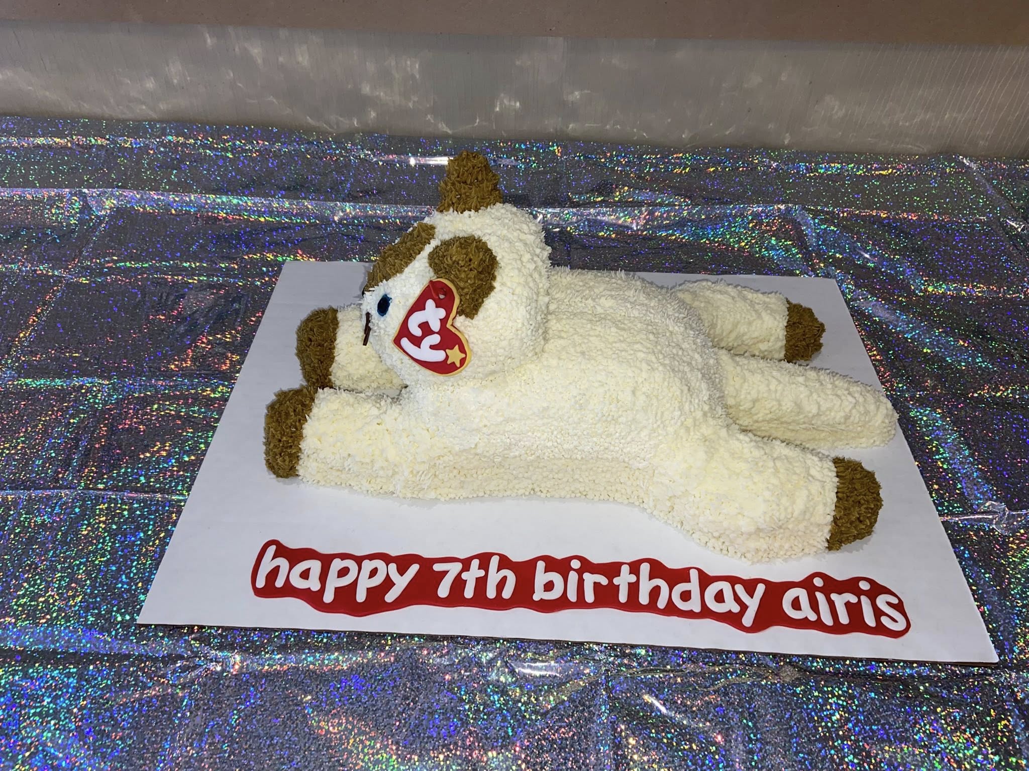 Beanie Baby cat-shaped birthday cake with a signature red heart tag and Happy 7th birthday Airis inscription.