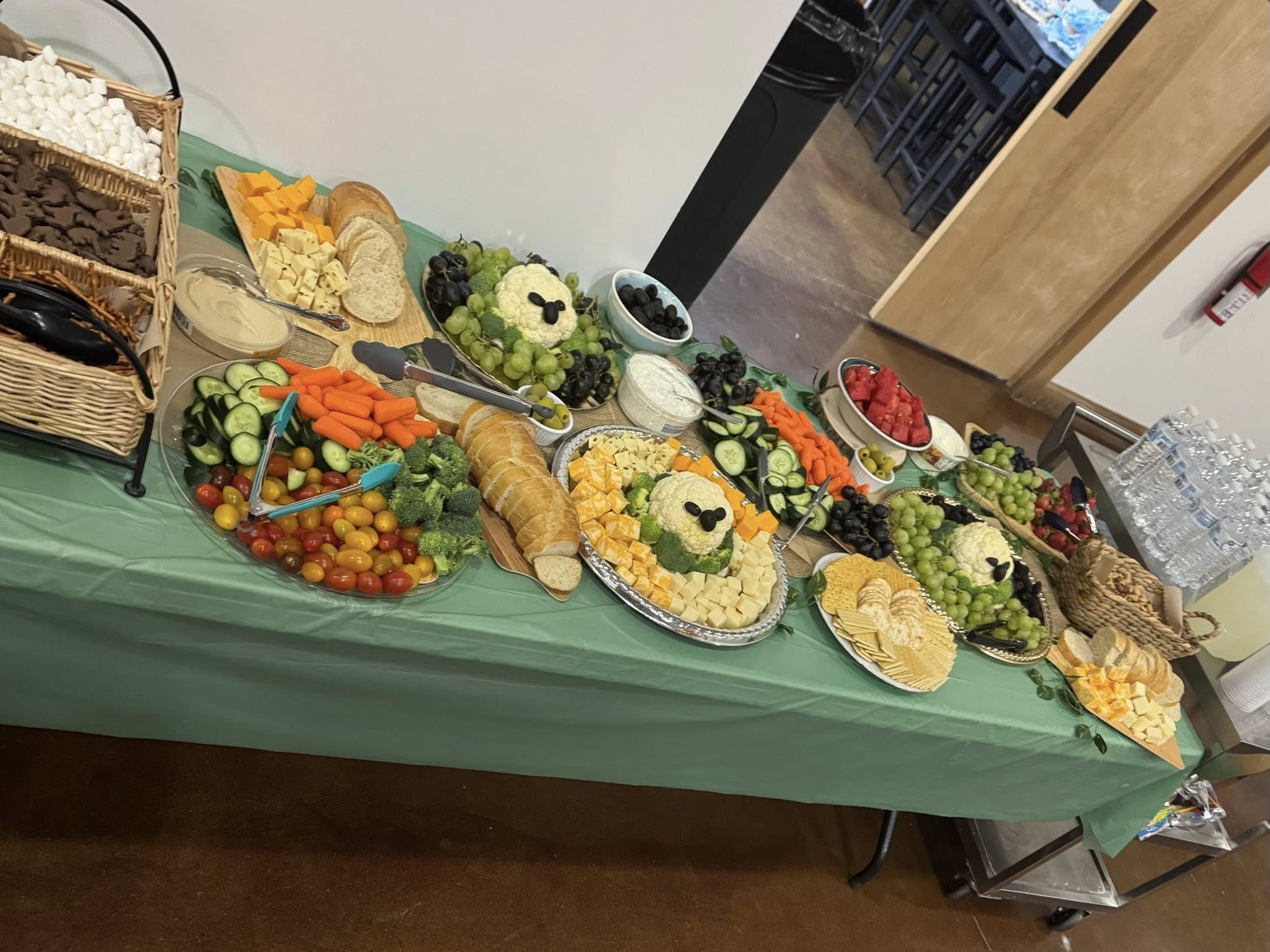 Table spread featuring various fresh vegetable platters, assorted cheeses, crackers, bread, and fruit.