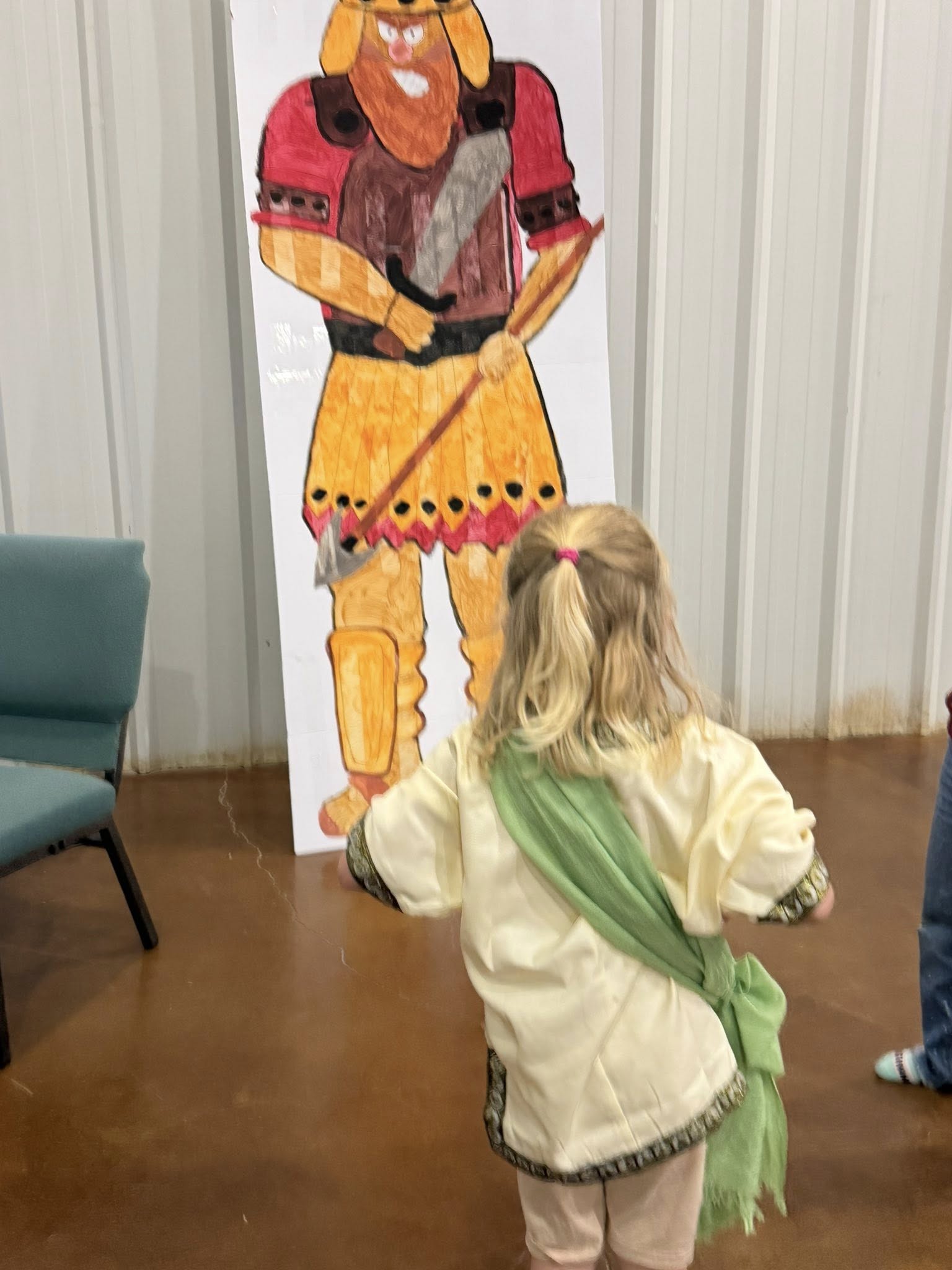 A young girl in a tunic looking at a large drawing of a warrior on a board