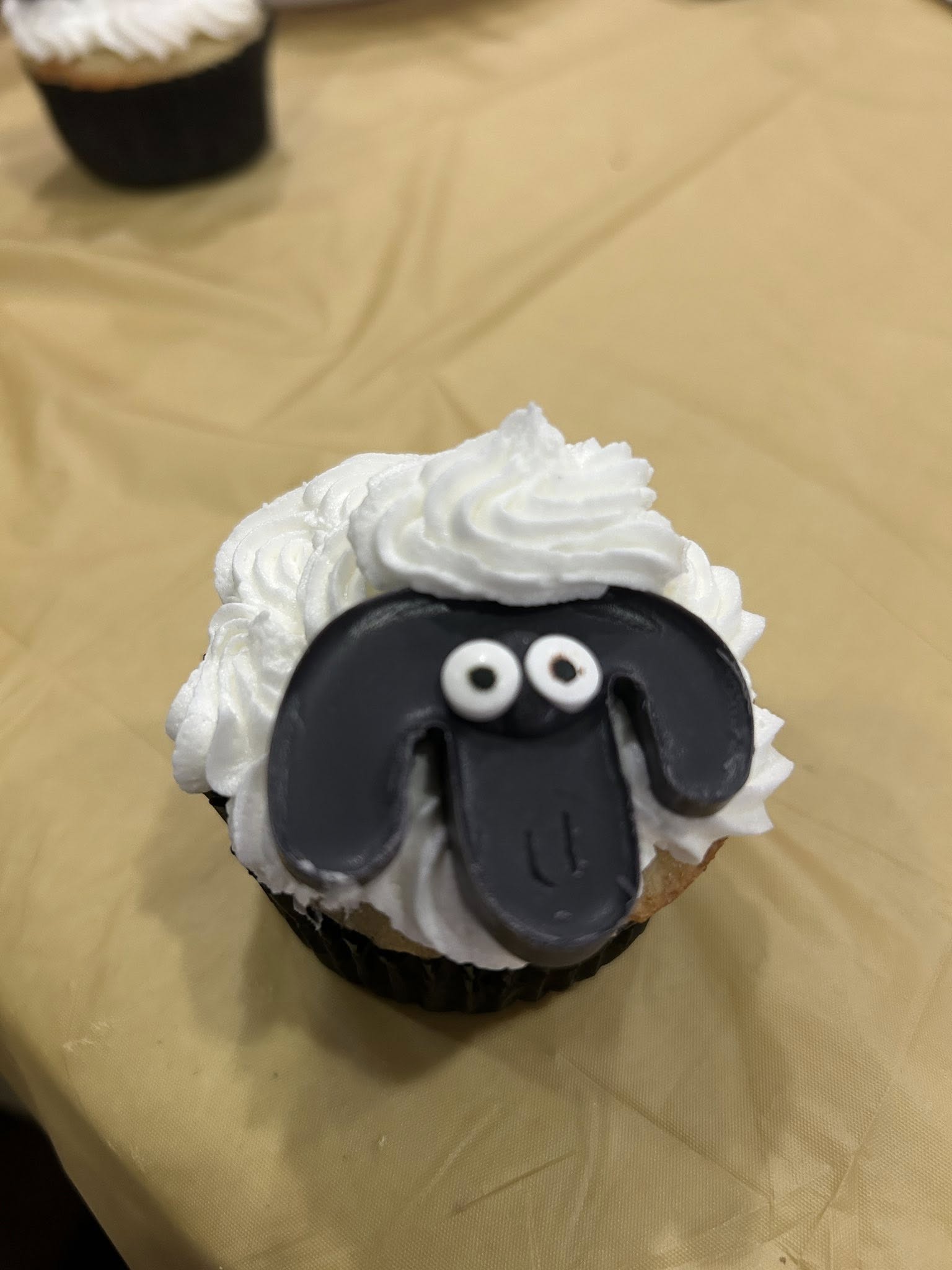 Cupcake decorated to look like Shaun the Sheep with white frosting fluff and a black fondant face