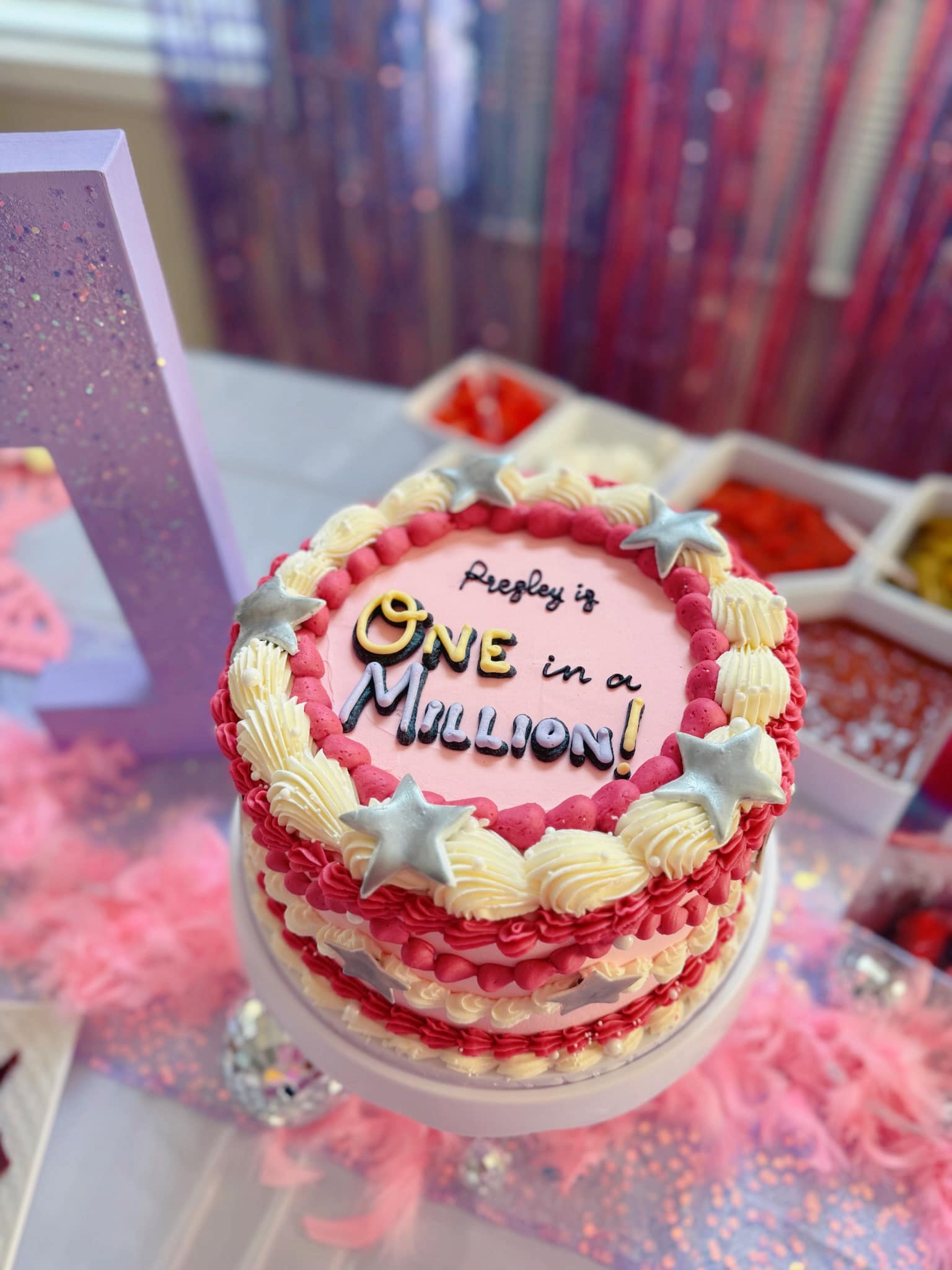 First birthday cake decorated with pink frosting, white trim, and silver stars, labeled Presley is One in a Million.