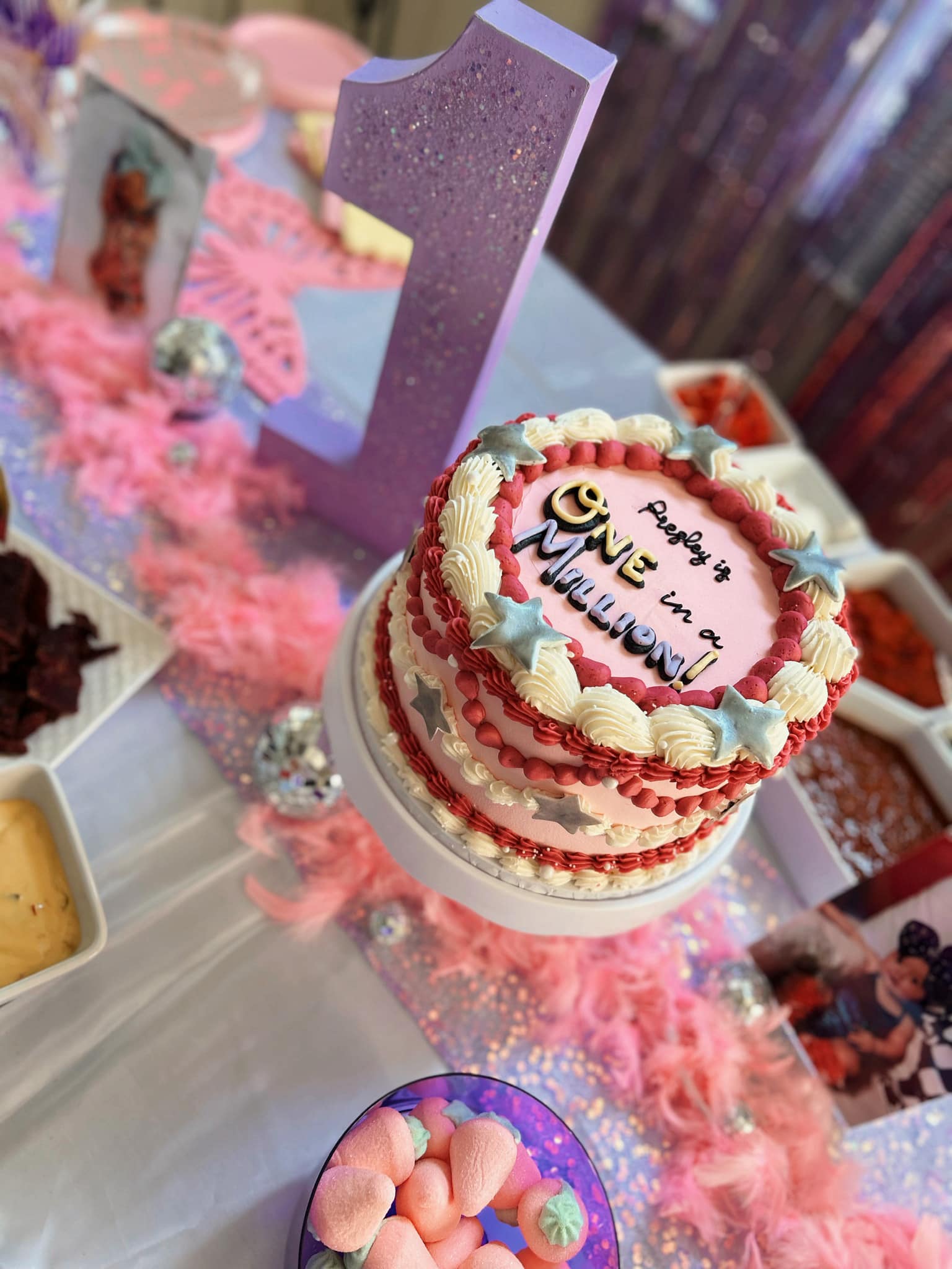 Pink birthday cake decorated with stars and the text Presley is ONE in a Million set for a first birthday party.