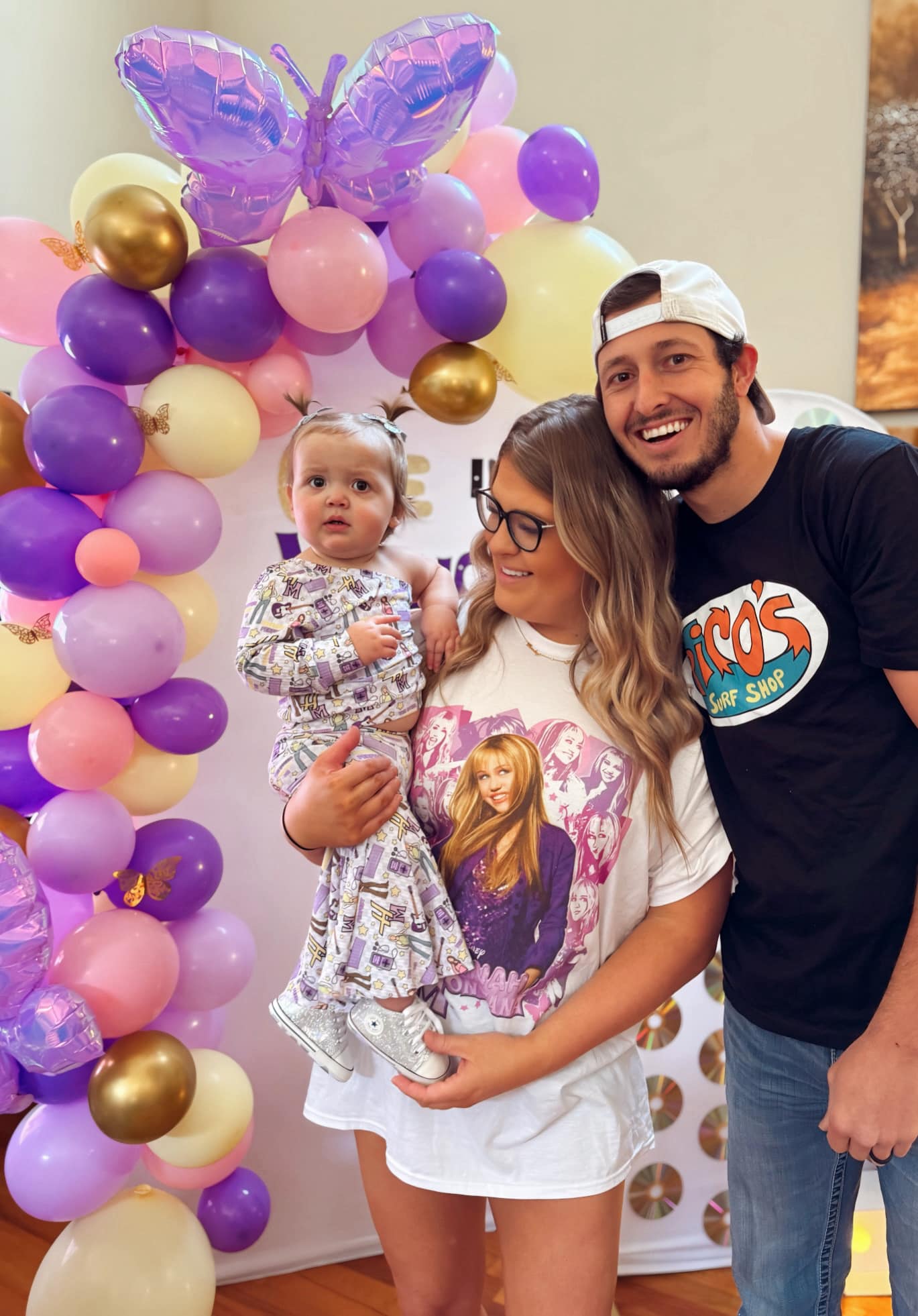 Family posing in front of a purple and cream balloon arch at a party.