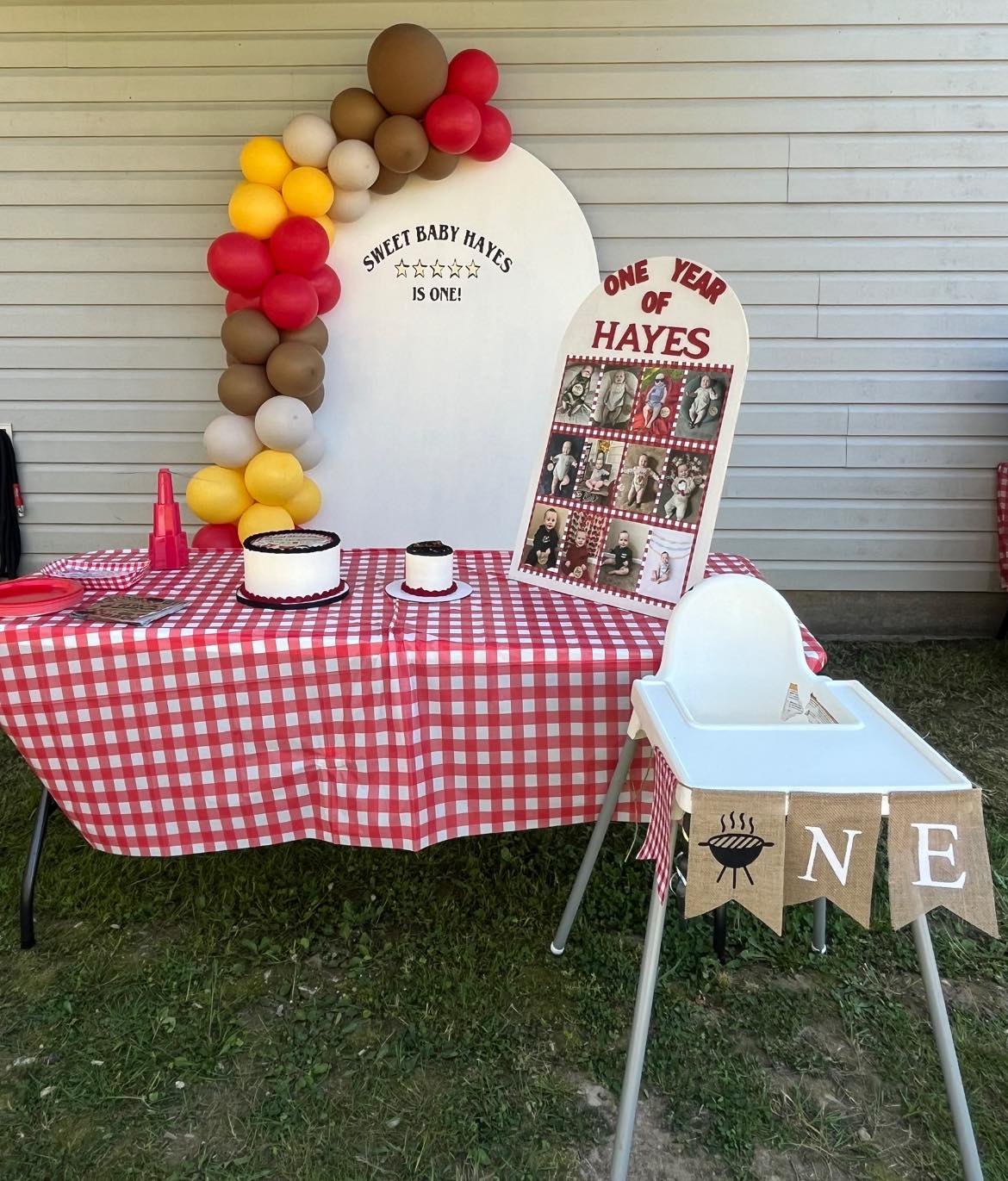 First birthday party decoration featuring a red and white checkered tablecloth, themed signage, and a balloon arch.