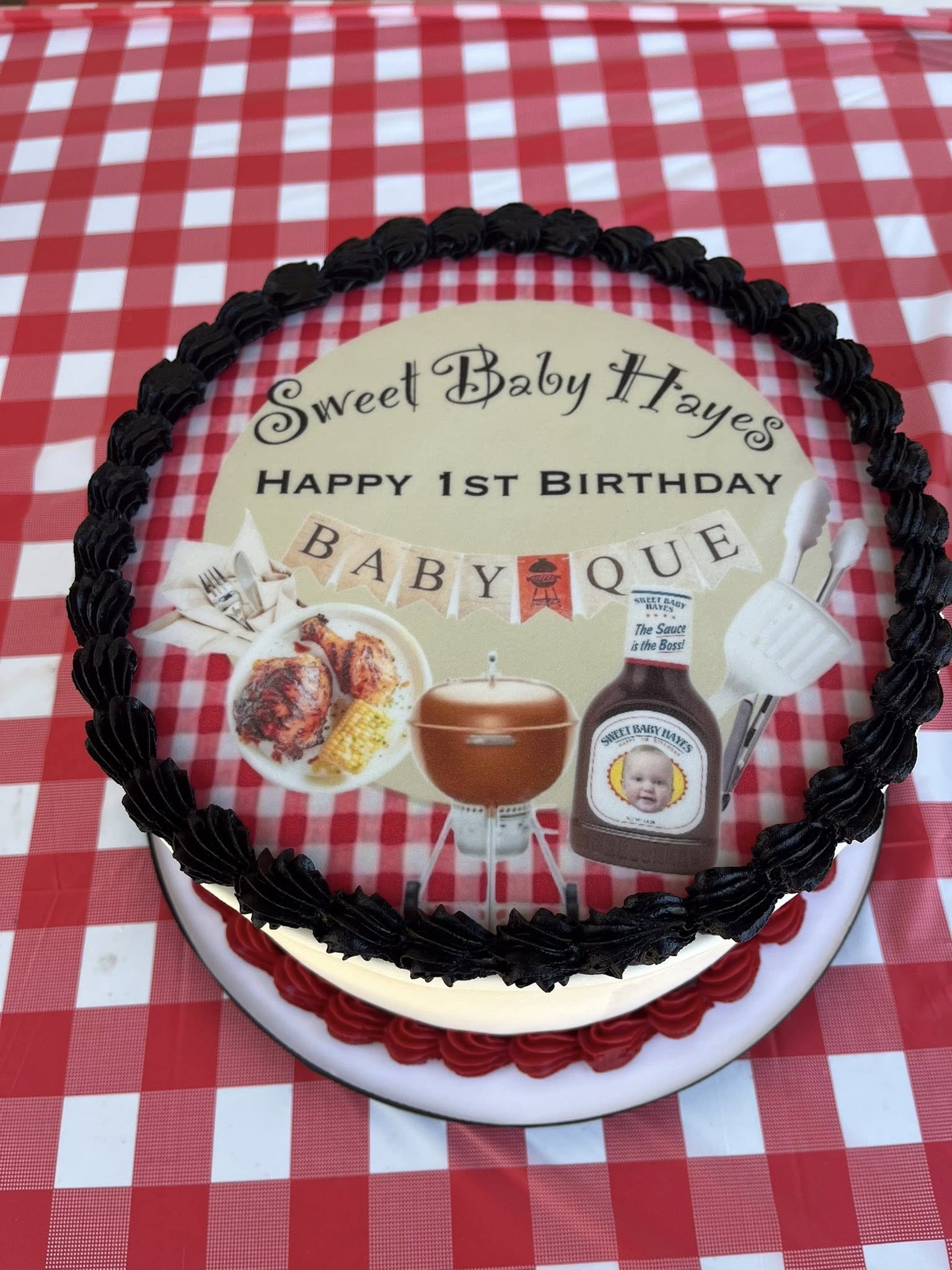 Round first birthday cake featuring a BBQ theme, grill graphics, and a custom Sweet Baby Hayes cake topper.