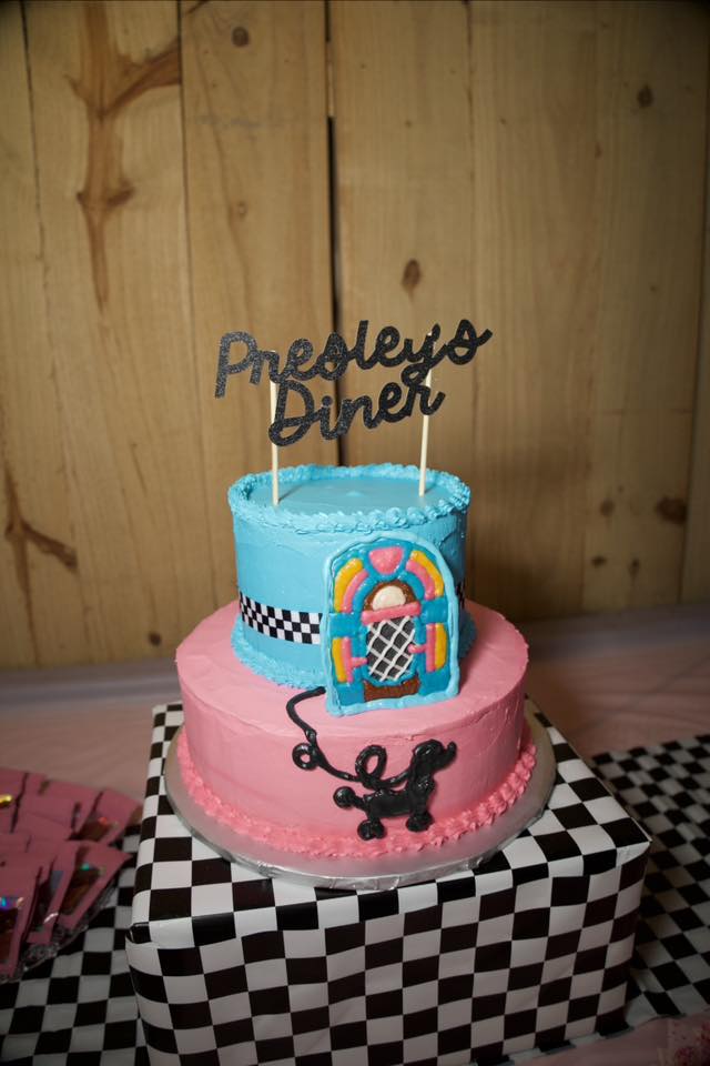 Two-tier blue and pink diner-themed cake decorated with a jukebox and poodle topper, labeled Presley's Diner.
