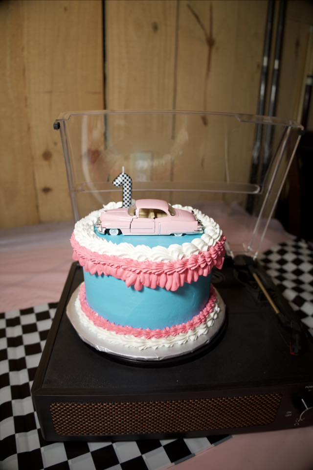 First birthday cake decorated with a toy pink car and a number one candle on a record player turntable.