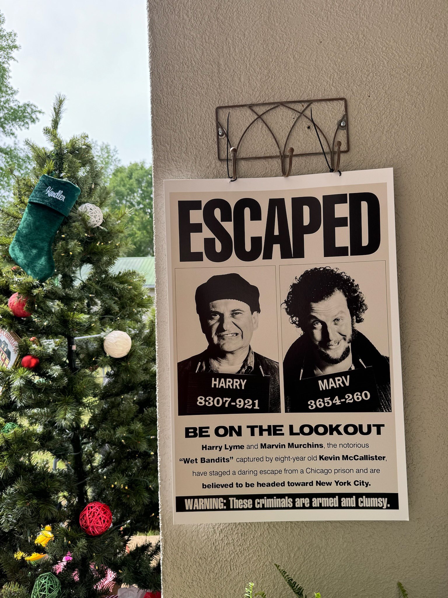 Home Alone Wet Bandits escaped wanted poster hanging on a wall next to a decorated Christmas tree.