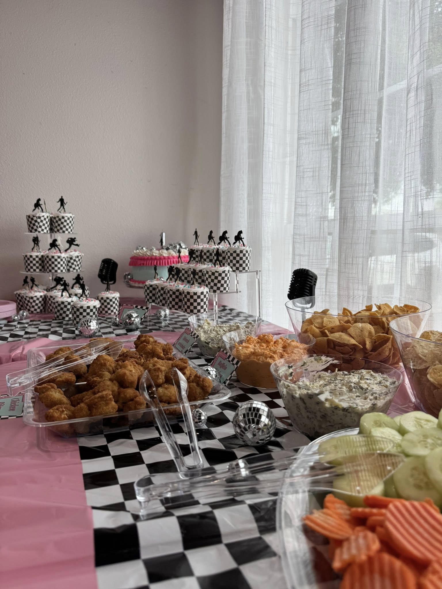 Table spread for a checkered-flag themed party with cupcakes, fried chicken, dip, and vegetable platters.