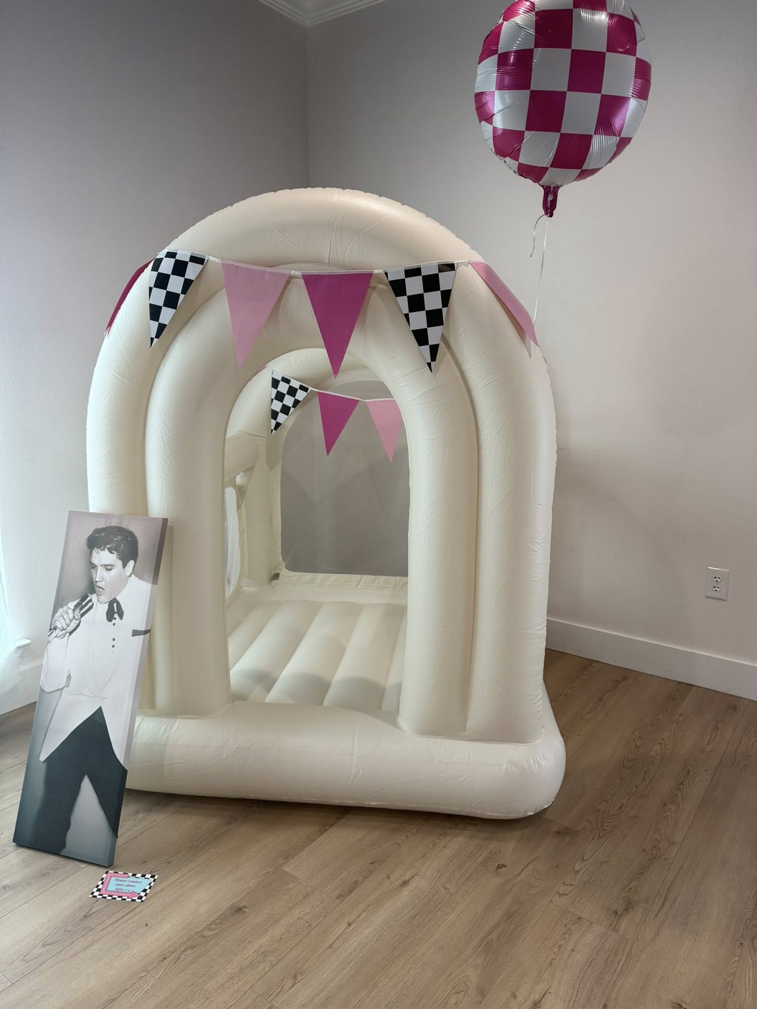 Cream-colored indoor bounce house decorated with pink and checkered pennant banners and matching checkerboard balloon