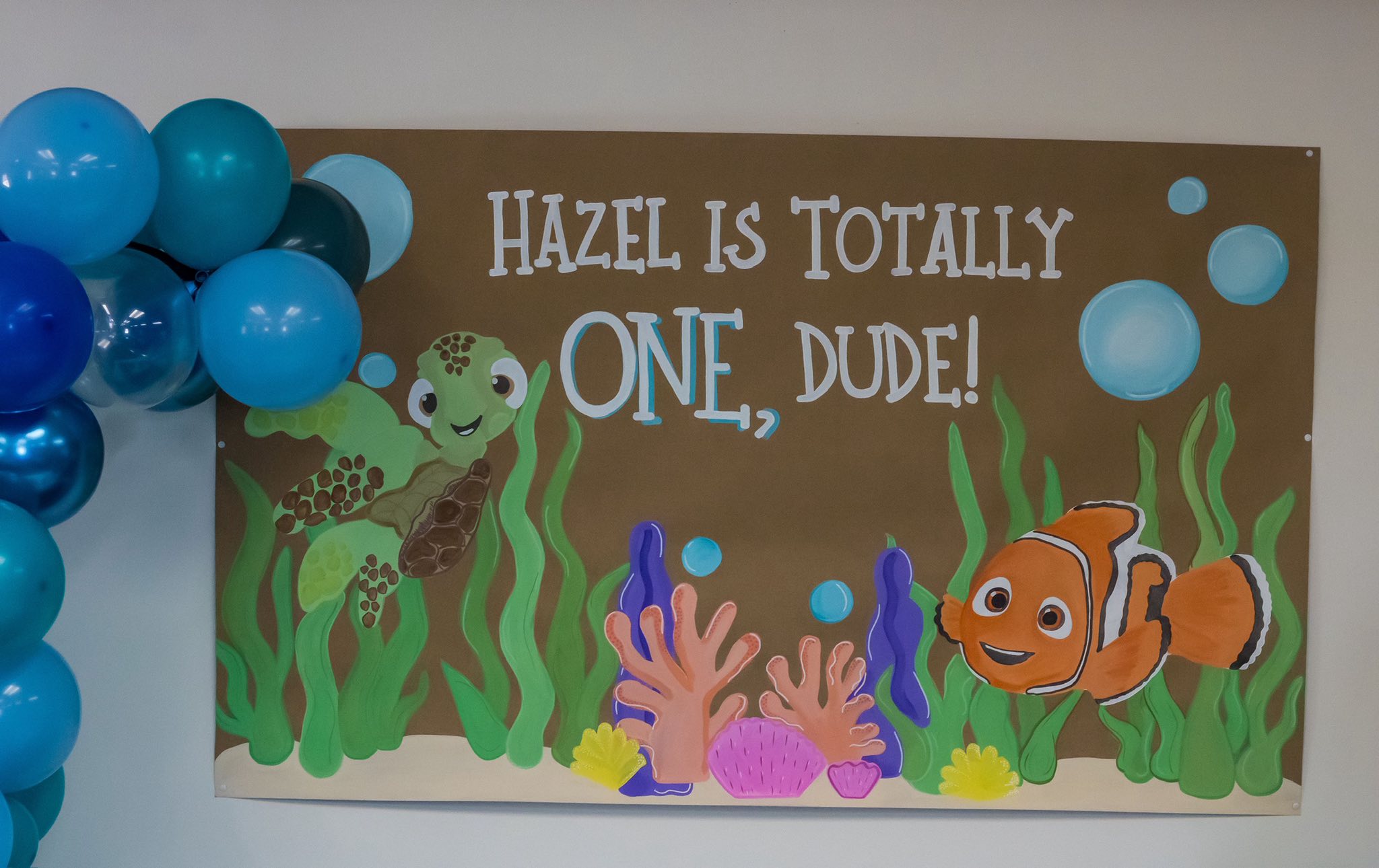 Personalized first birthday party banner featuring a sea turtle and clownfish illustration with the text Hazel Is Totally One, Dude!