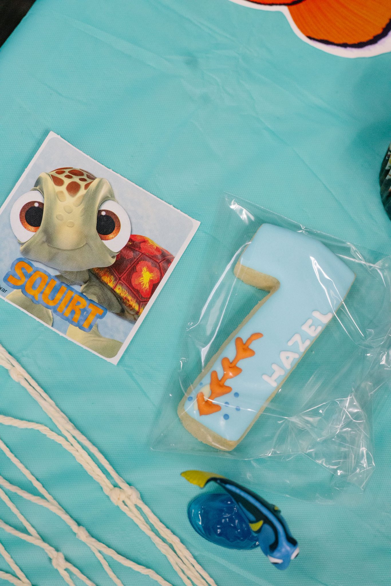 First birthday cookie shaped as a number one, decorated with the name Hazel and sea-themed accents next to a Squirt character card.