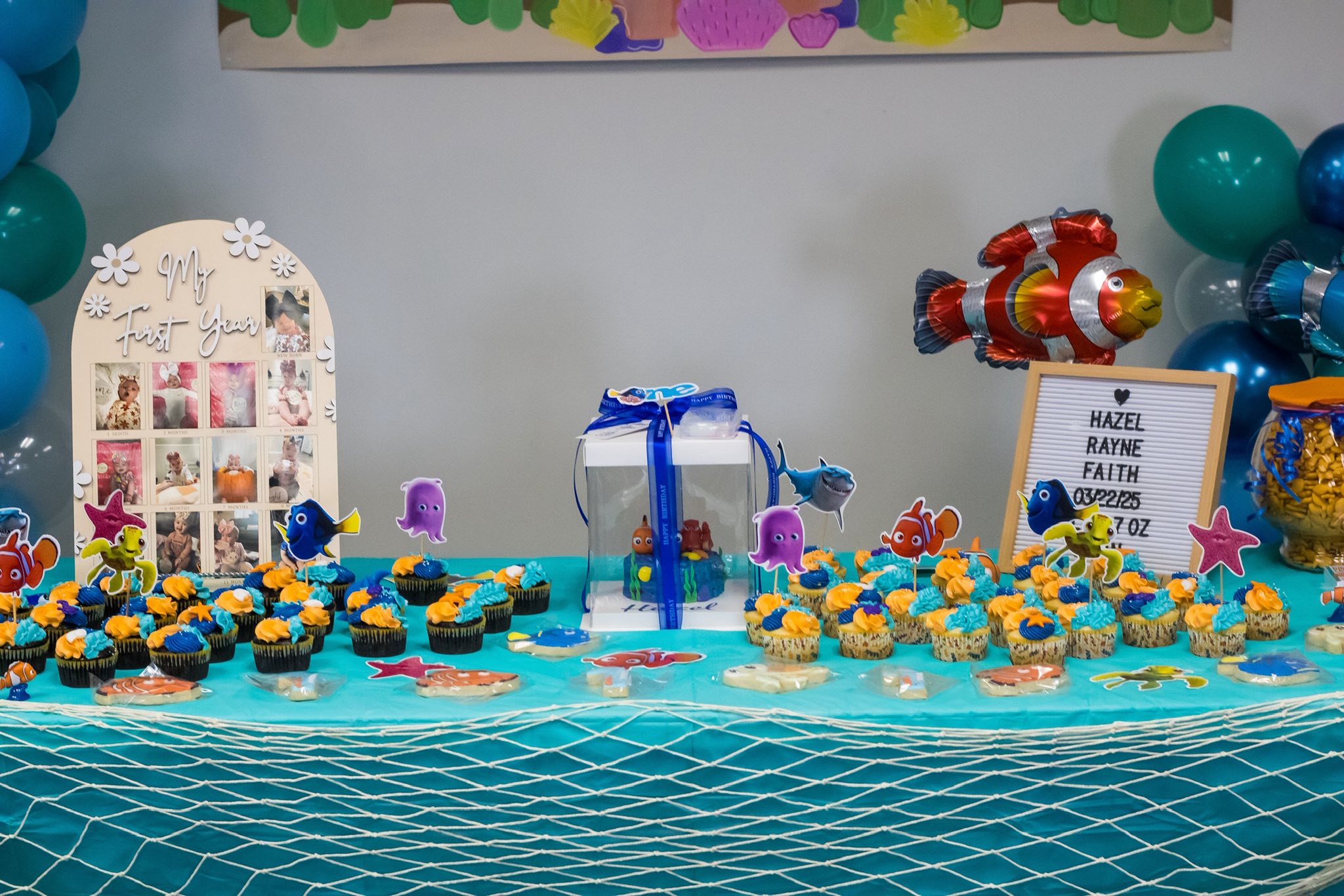 Table set up for Finding Nemo themed first birthday with cupcakes, custom photo board, and personalized sign.