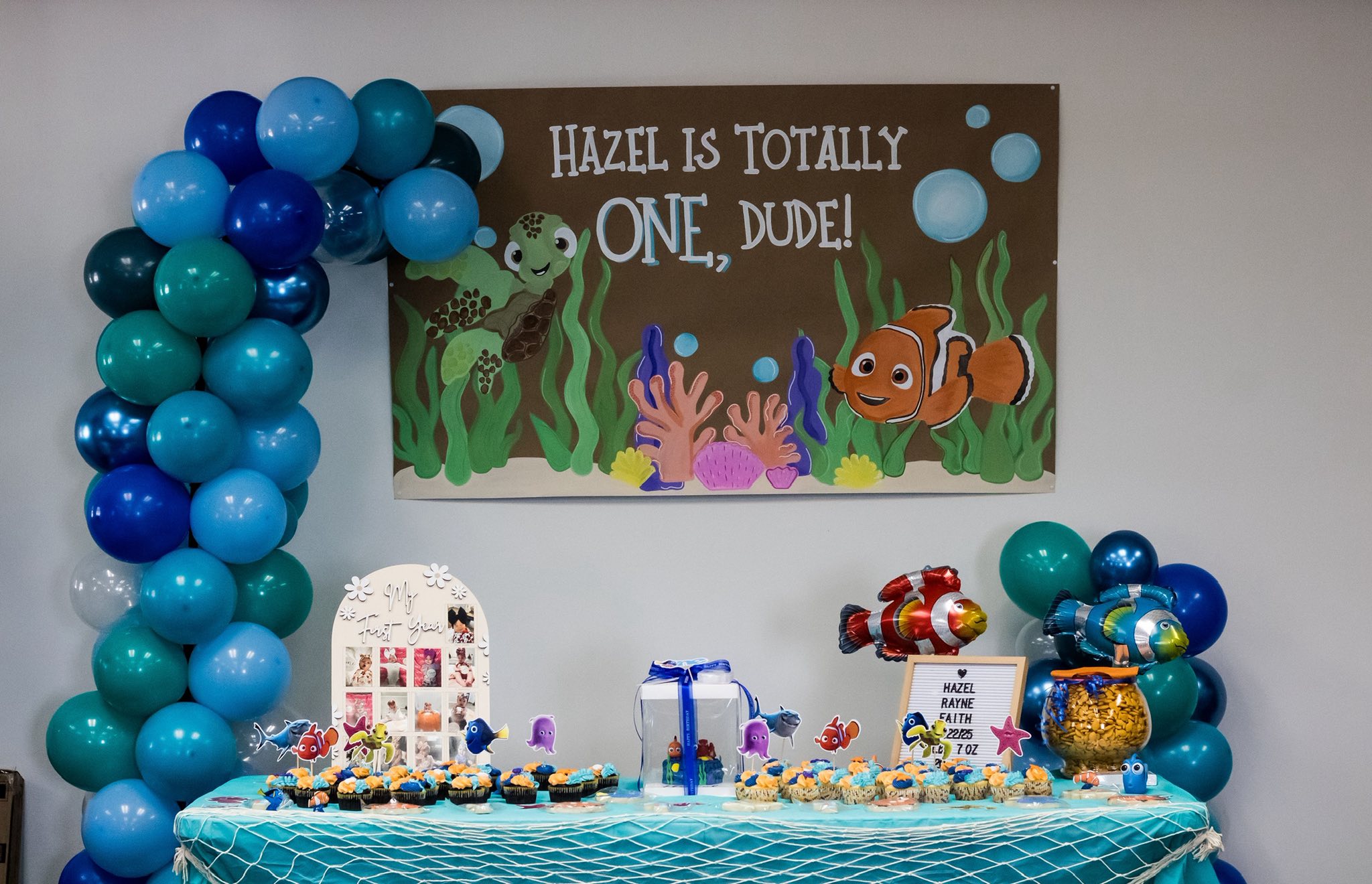 Finding Nemo themed first birthday party table with blue balloon arch and cupcakes.