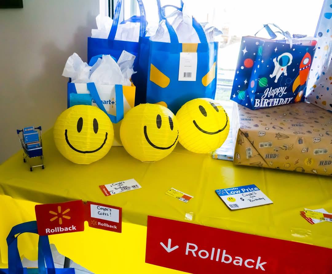 Table styled with smiley face lanterns, party gift bags, and Walmart-themed Rollback birthday signage.