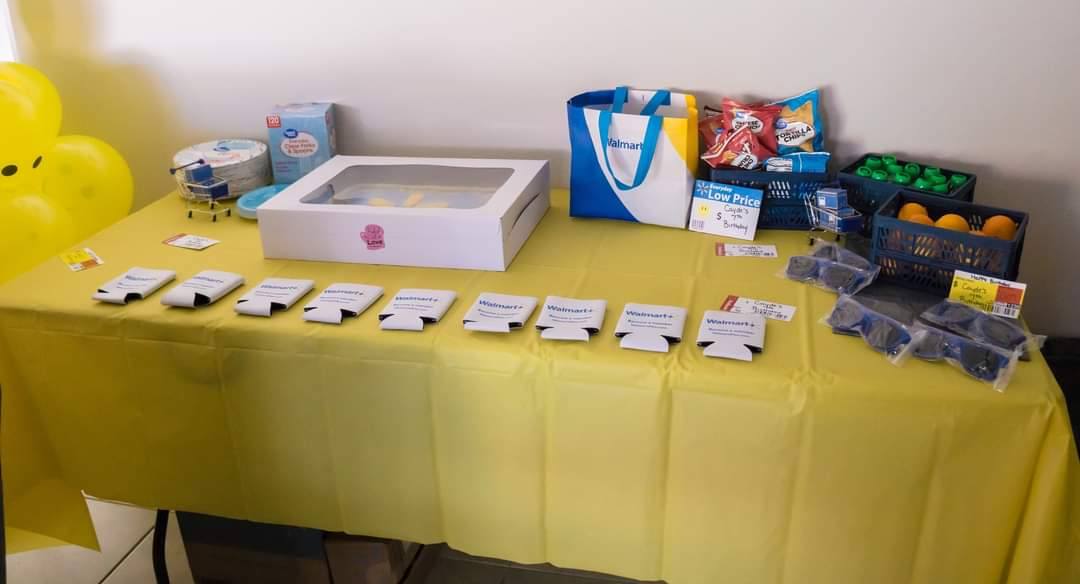 A yellow-covered party table displaying Walmart-themed favors, snacks, and party supplies.