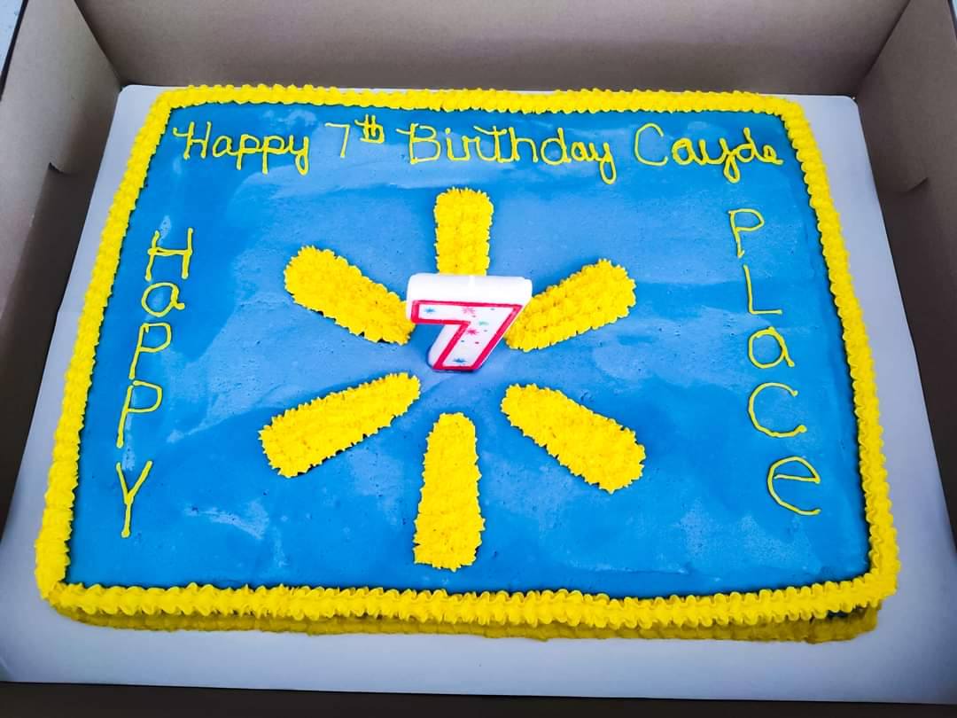 Rectangular sheet cake with blue icing, yellow trim, and a Walmart spark logo design, topped with a number 7 candle.