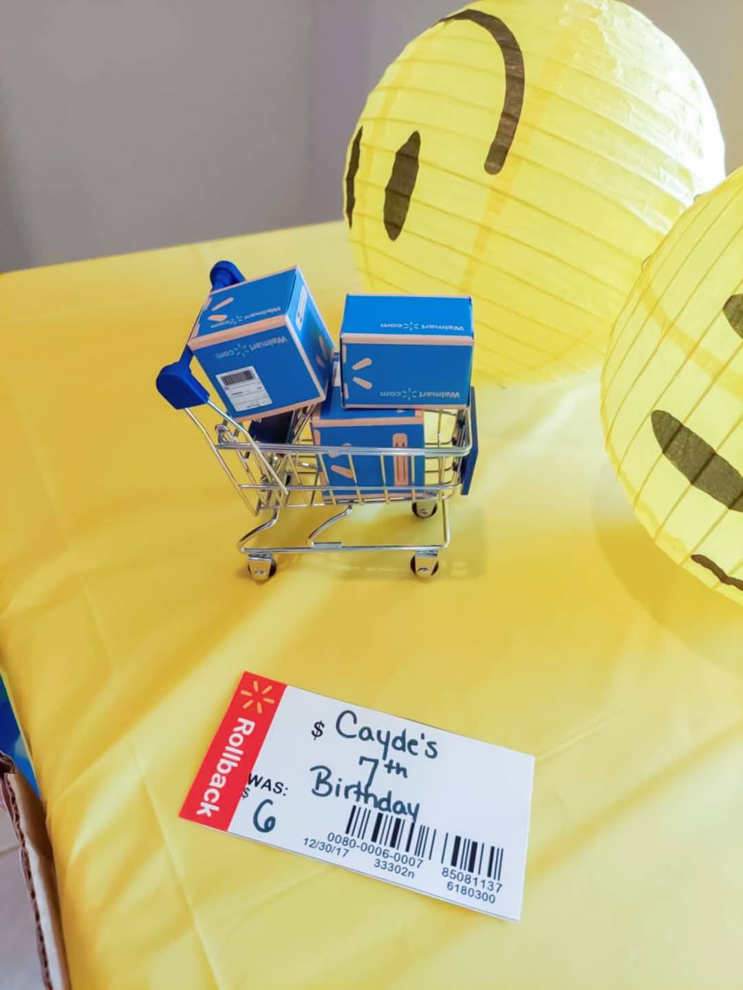 Miniature Walmart shopping cart filled with toy boxes next to a custom Rollback birthday sign.