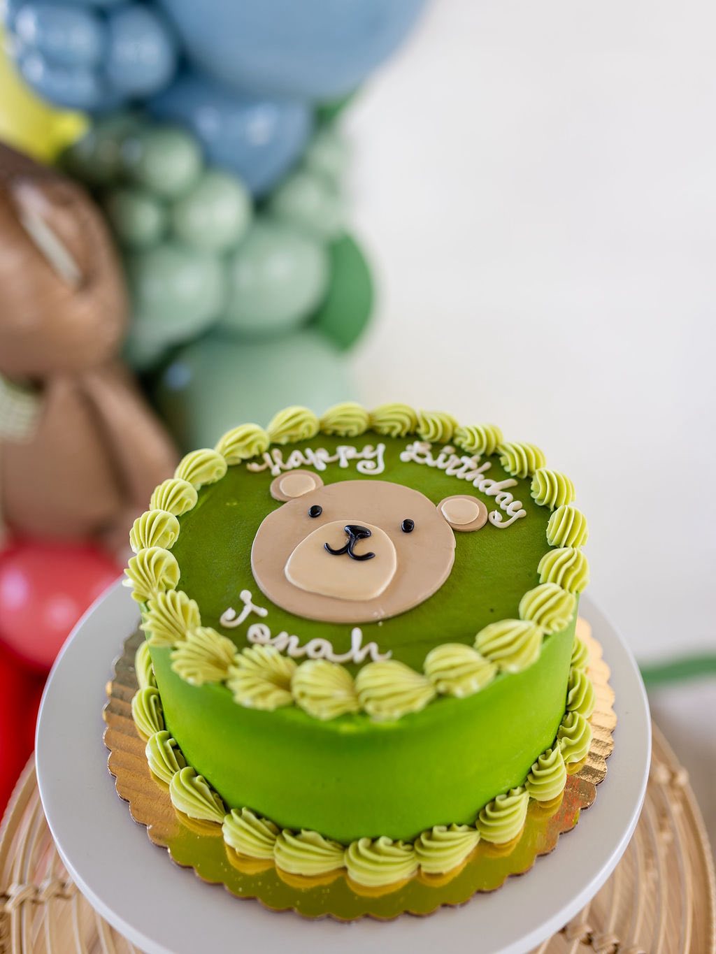 Green birthday cake with a teddy bear topper and the name Jonah written in icing.