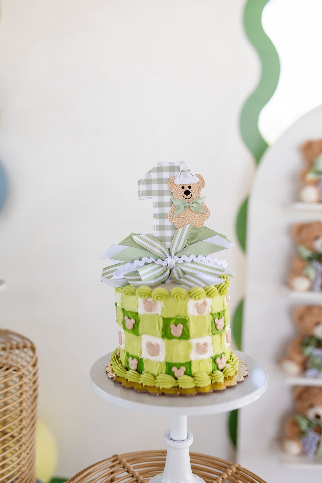 First birthday cake decorated with light green gingham patterns, teddy bear accents, and a number one topper.