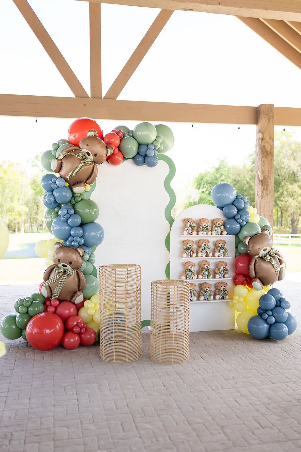 Teddy bear themed party setup with colorful balloon garland, backdrop, and small teddy bear party favors.